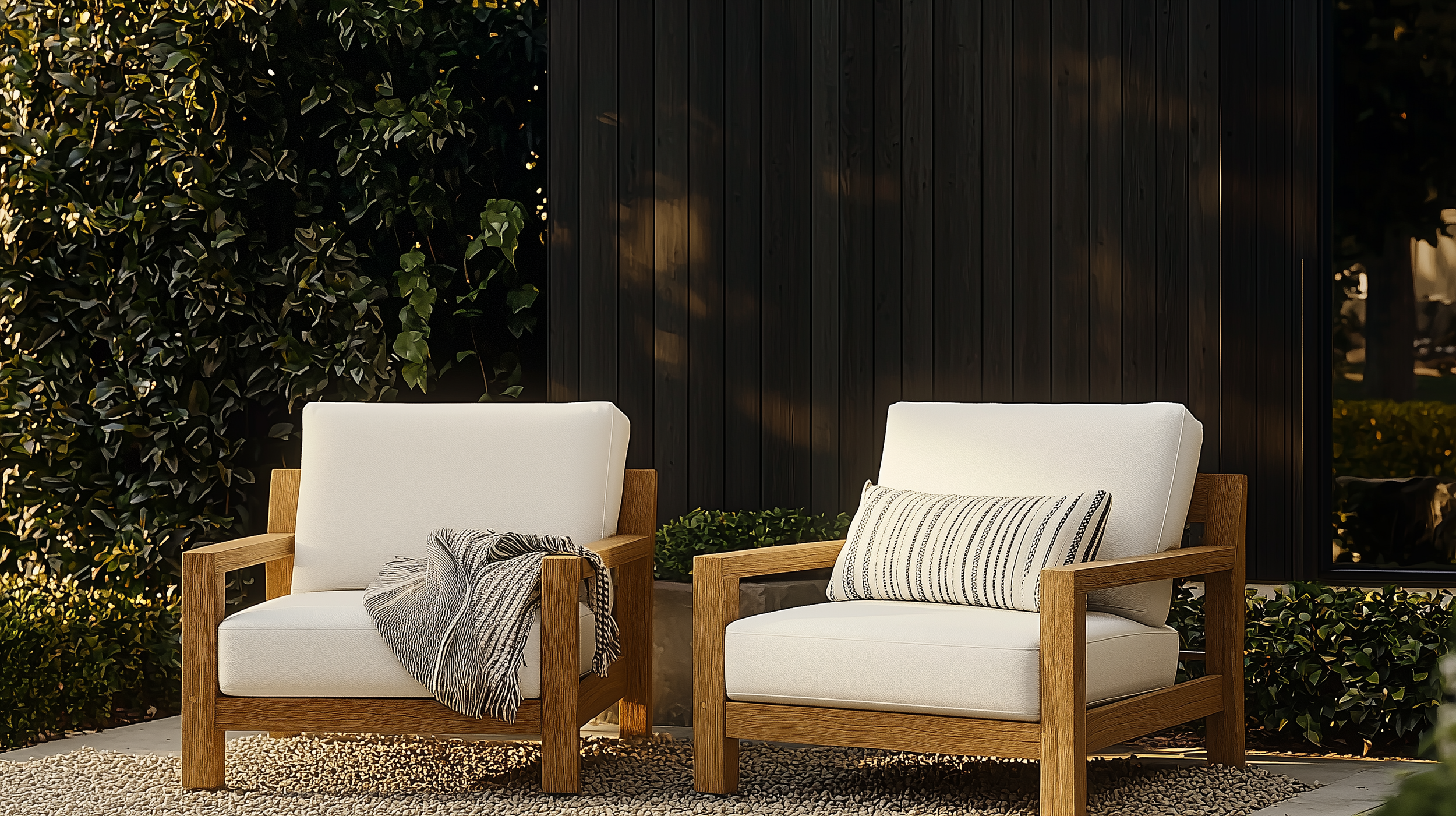 An inviting outdoor seating area featuring two modern teak armchairs with clean, angular frames and plush white cushions, inspired by high-end minimalist patio furniture.