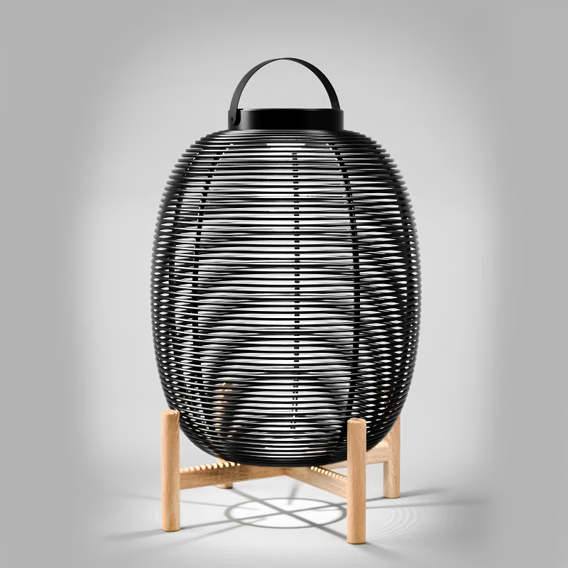 A solar-powered black woven basket LED lantern that is crafted using the 'Lloyd Loom' technique. Where Kraft paper is twisted around metal wire and woven into unique furniture pieces. Set against a neutral grey background.