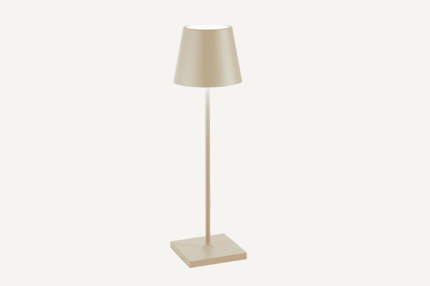 A golden color indoor/outdoor cordless rechargeable led table lamp with a long, skinny, die-cast aluminum body and shade mounted on a square base, set against a neutral colored backdrop.