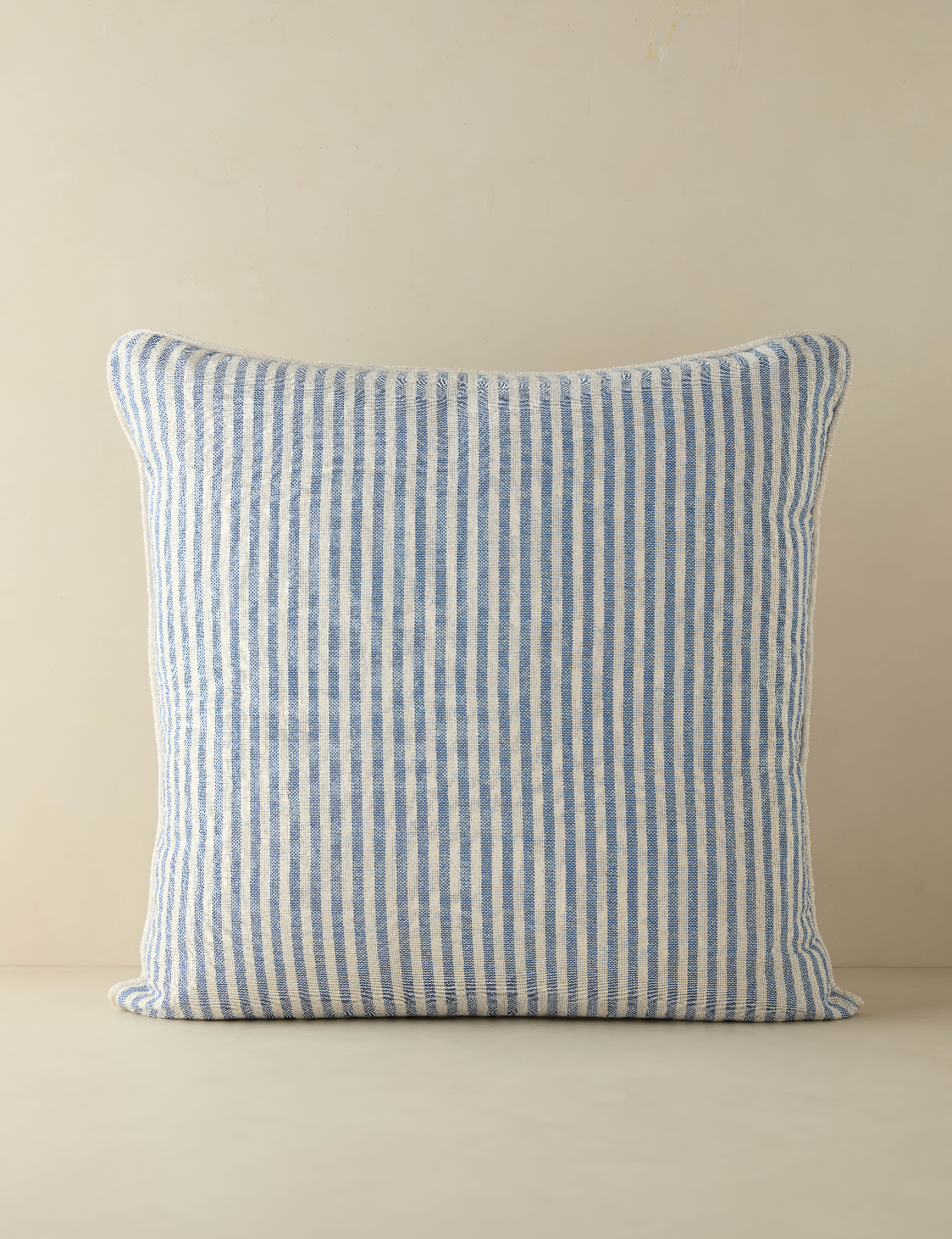 Gorgeous striped pillow in pastel variations of white and blue set on a dark cream background.