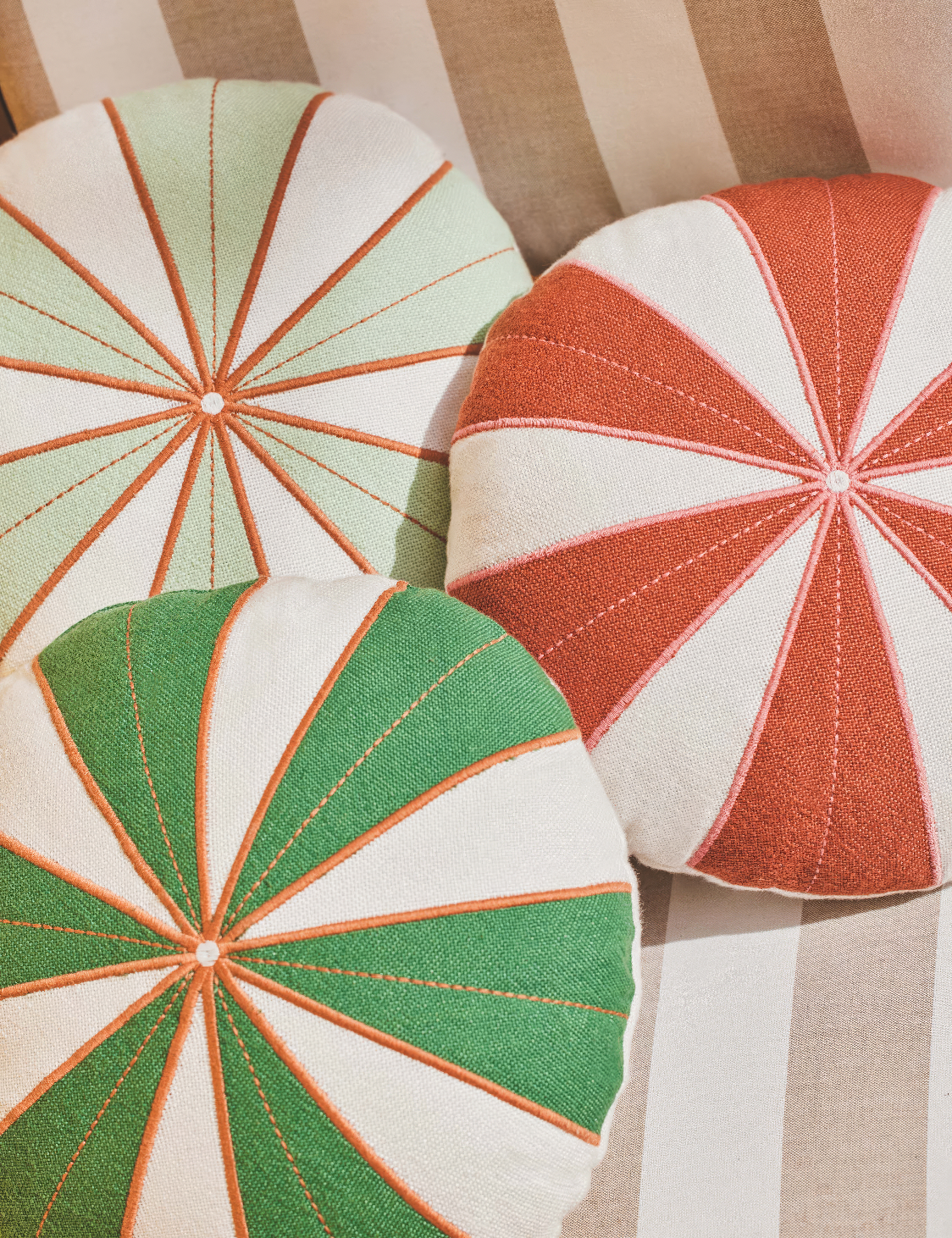 A trio of round, pinwheel-patterned pillows in green, mint, and burnt orange with cream accents. Each pillow features a stitched radial design converging at a central button, creating a playful, vintage-inspired look. Perfect for adding a pop of colo
