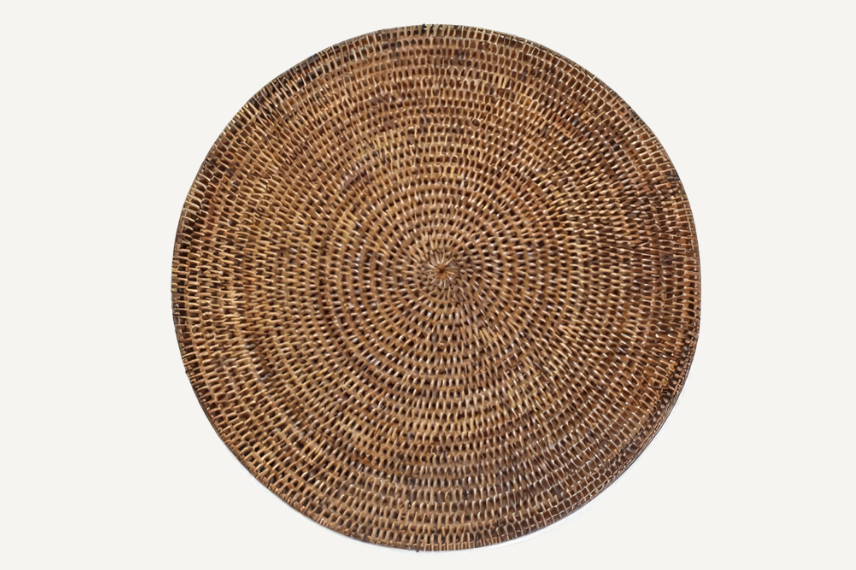 Round woven rattan placemat with a tight, intricate weave in warm natural brown tones. The handcrafted design adds a rustic yet elegant touch to any dining table, perfect for casual or formal settings.