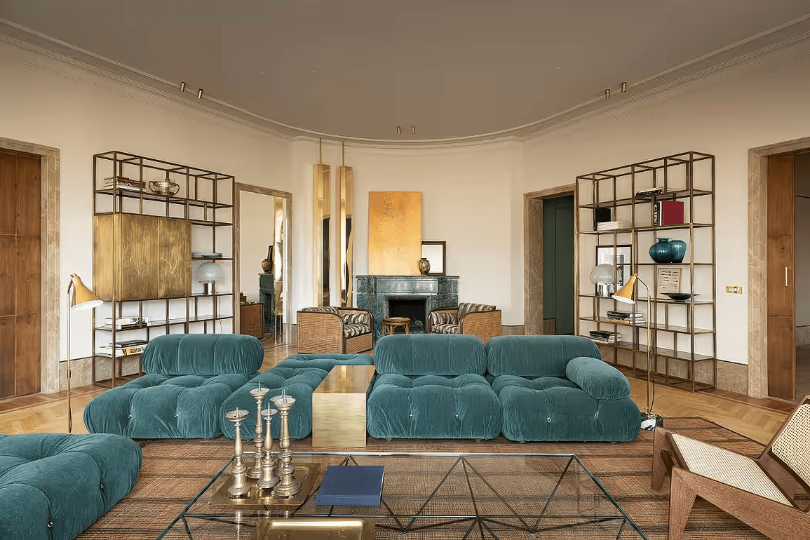 Elegant living room with teal tufted sofas, gold accents, and open shelving.