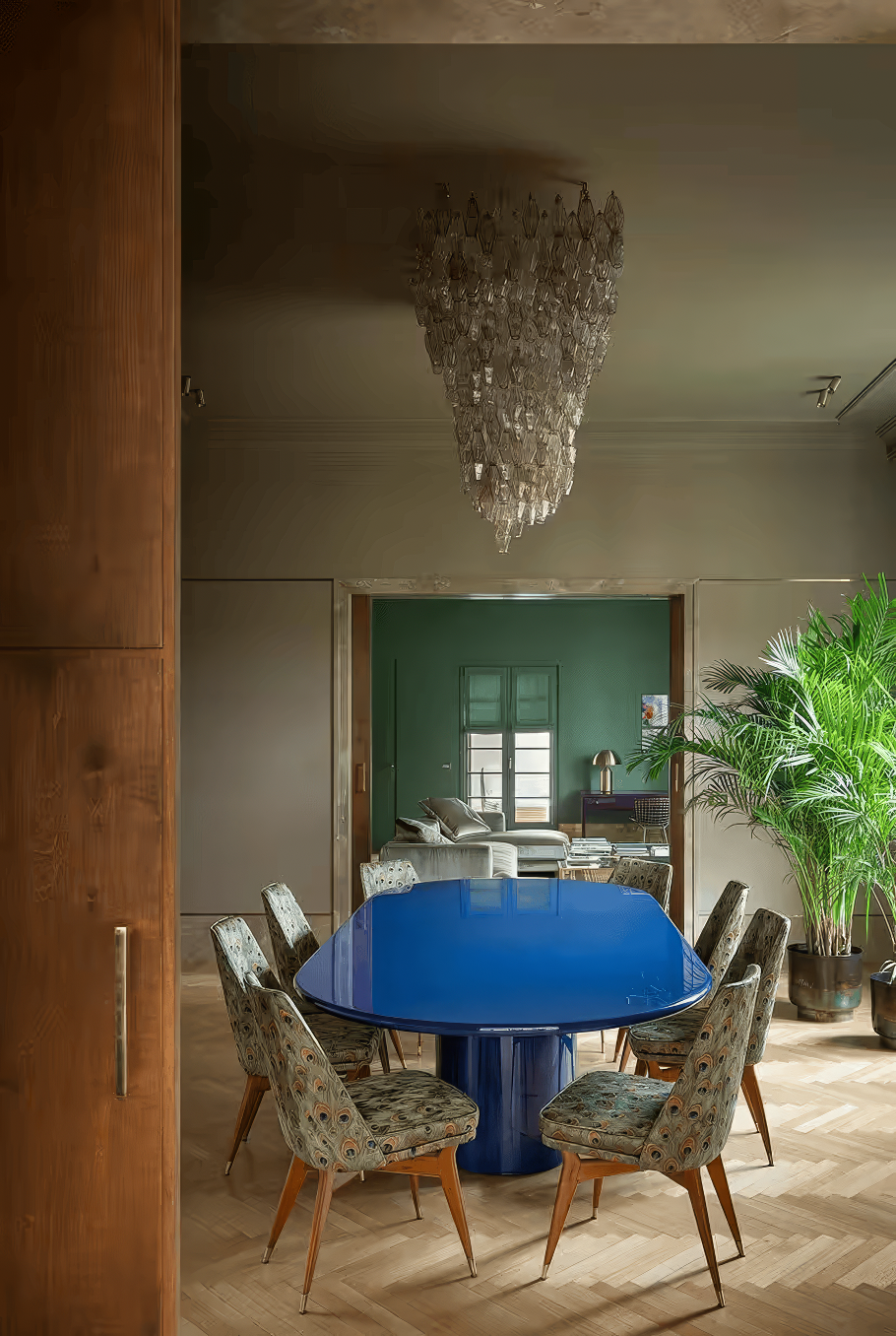 Dining room with bold cobalt blue table, peacock-print chairs, and a statement chandelier.