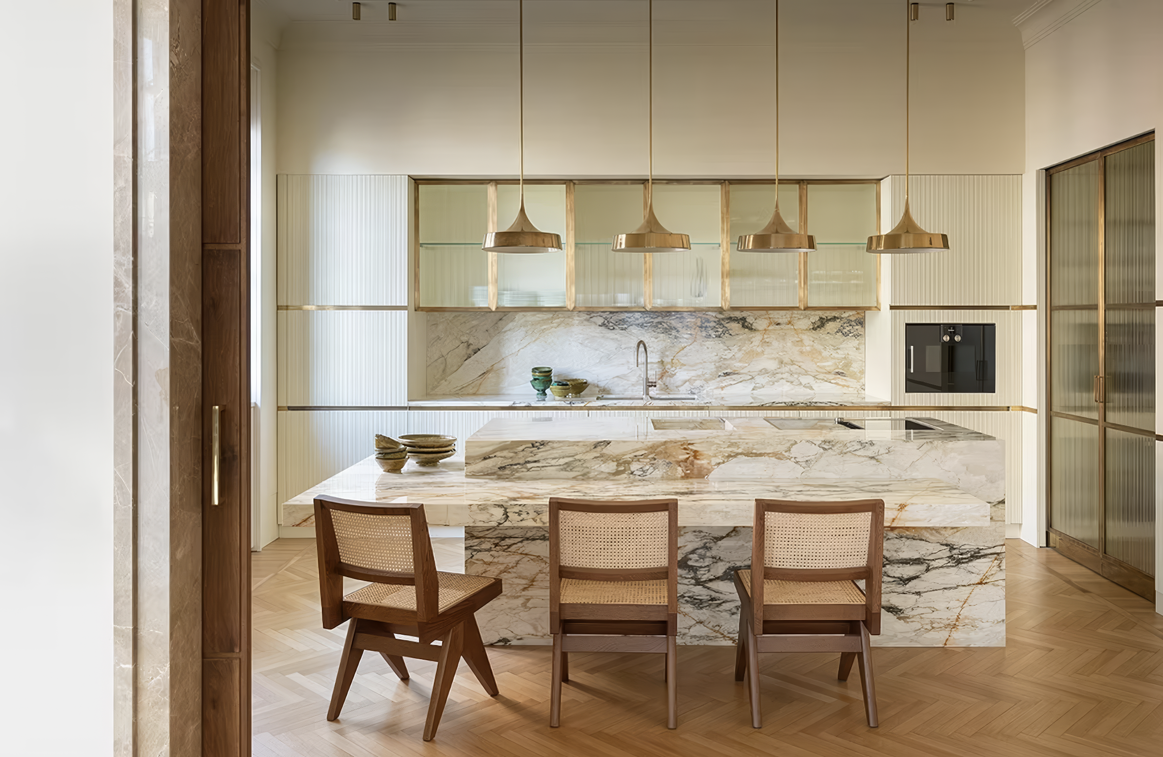 Modern kitchen with waterfall marble island, gold pendant lighting, and cane-back chairs.