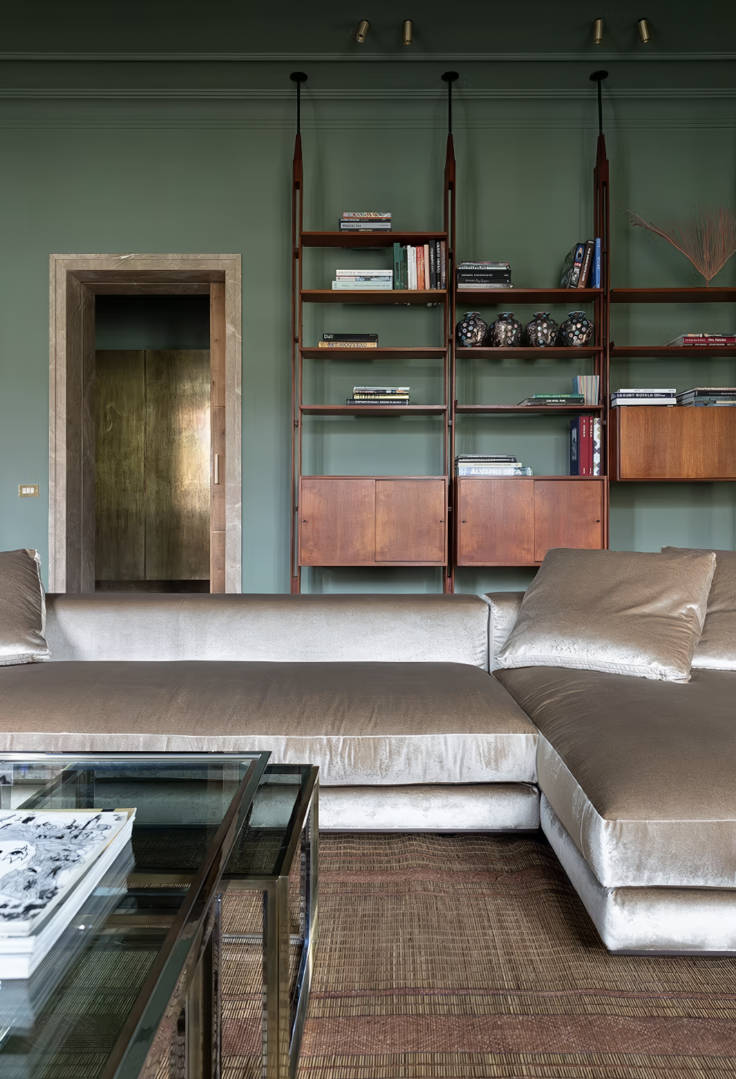 Green living room with low velvet sectional and mid-century style bookshelf.