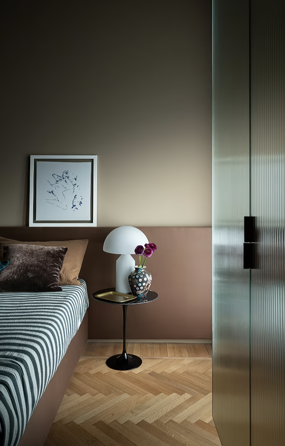Modern bedroom with striped bedding, sculptural lamp, and framed abstract art.