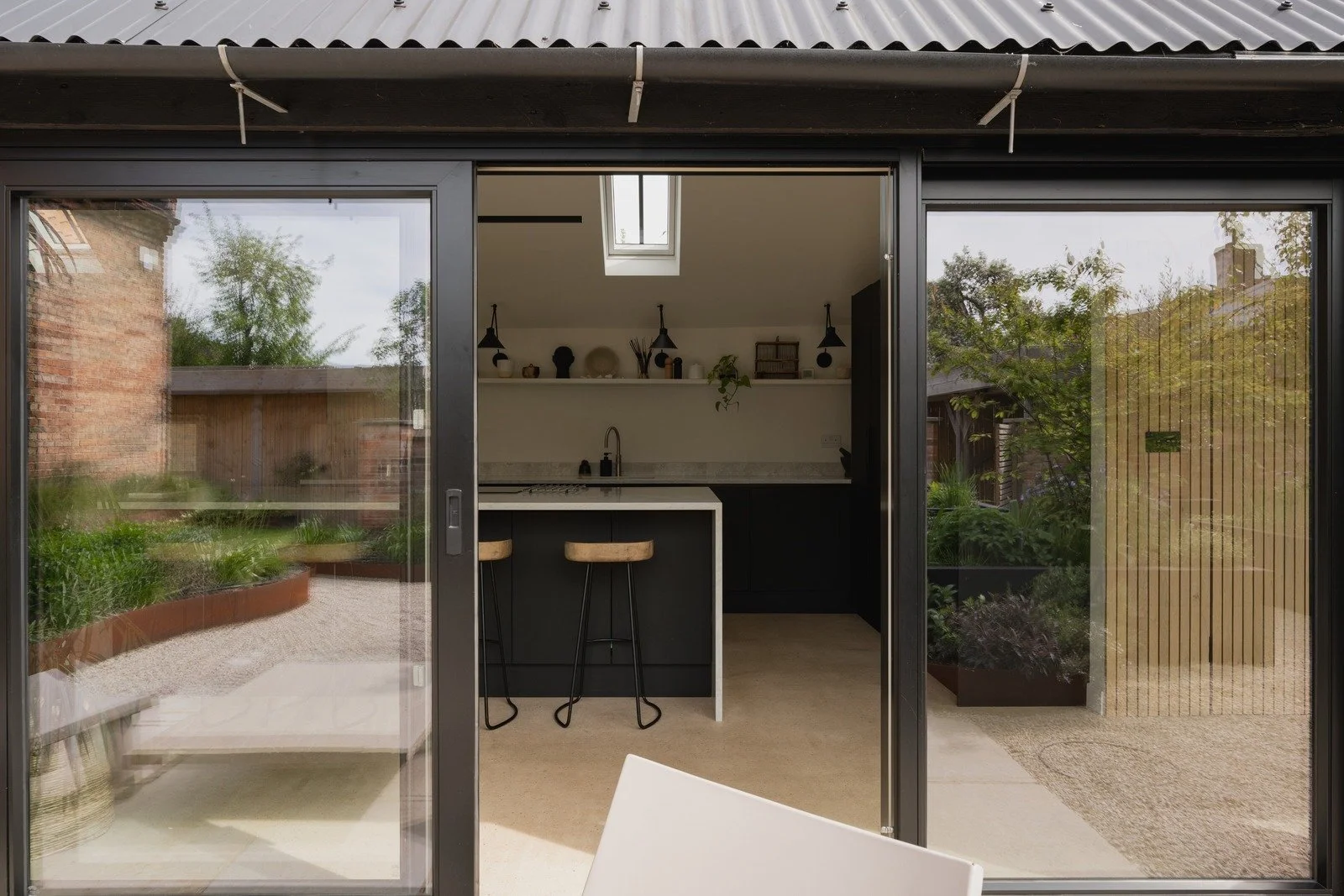 Kitchenette with open shelving and breakfast bar seen from the garden through wide glass sliding doors at Fen Barn.