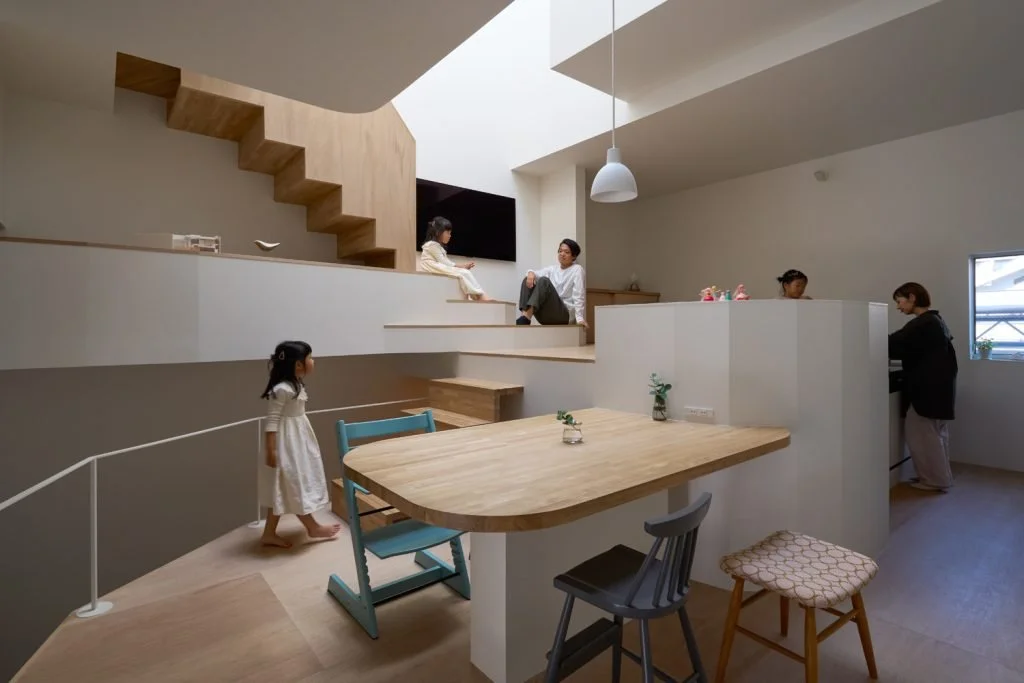 View of a modern Japanese interior showing children playing near a dining area and staircase while adults cook and chat.