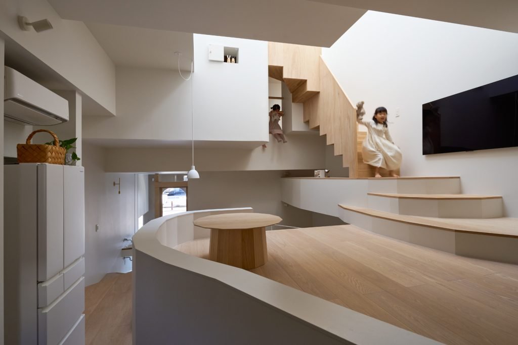 Kids playing energetically on a curved staircase platform in a multi-level home filled with architectural light and movement.