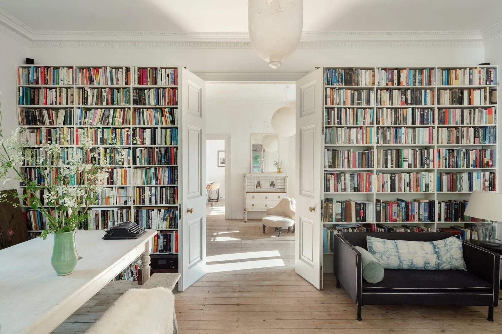 Reception room with floor-to-ceiling library and large white dining room table with a sofa in front of the books.