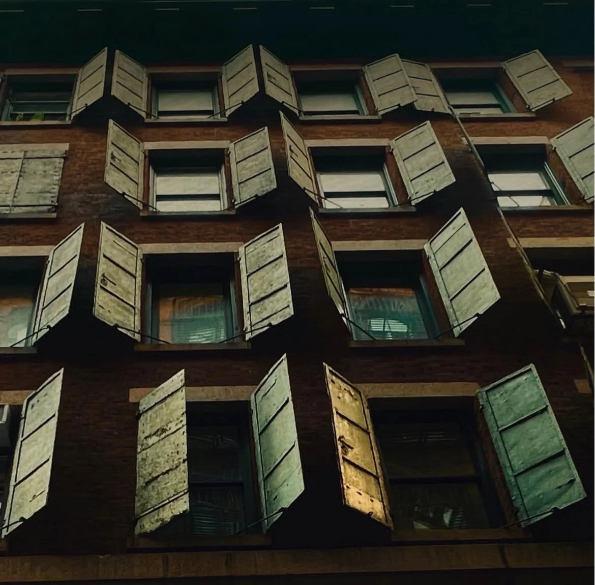 A close-up view of a brick building with multiple windows and open green shutters.
