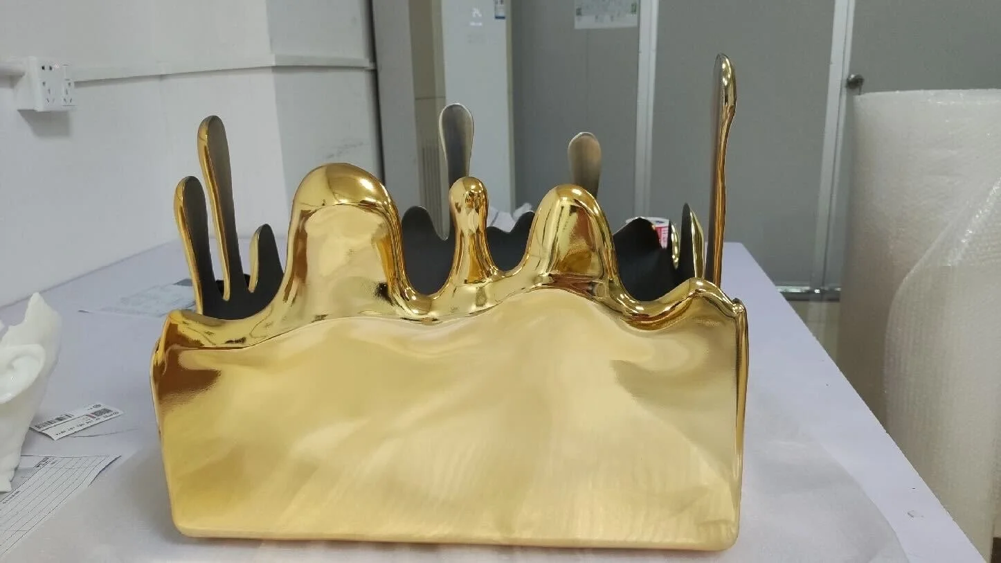 A gold-colored decorative object with an irregular, dripping design, positioned on a table with background office or storage setting.