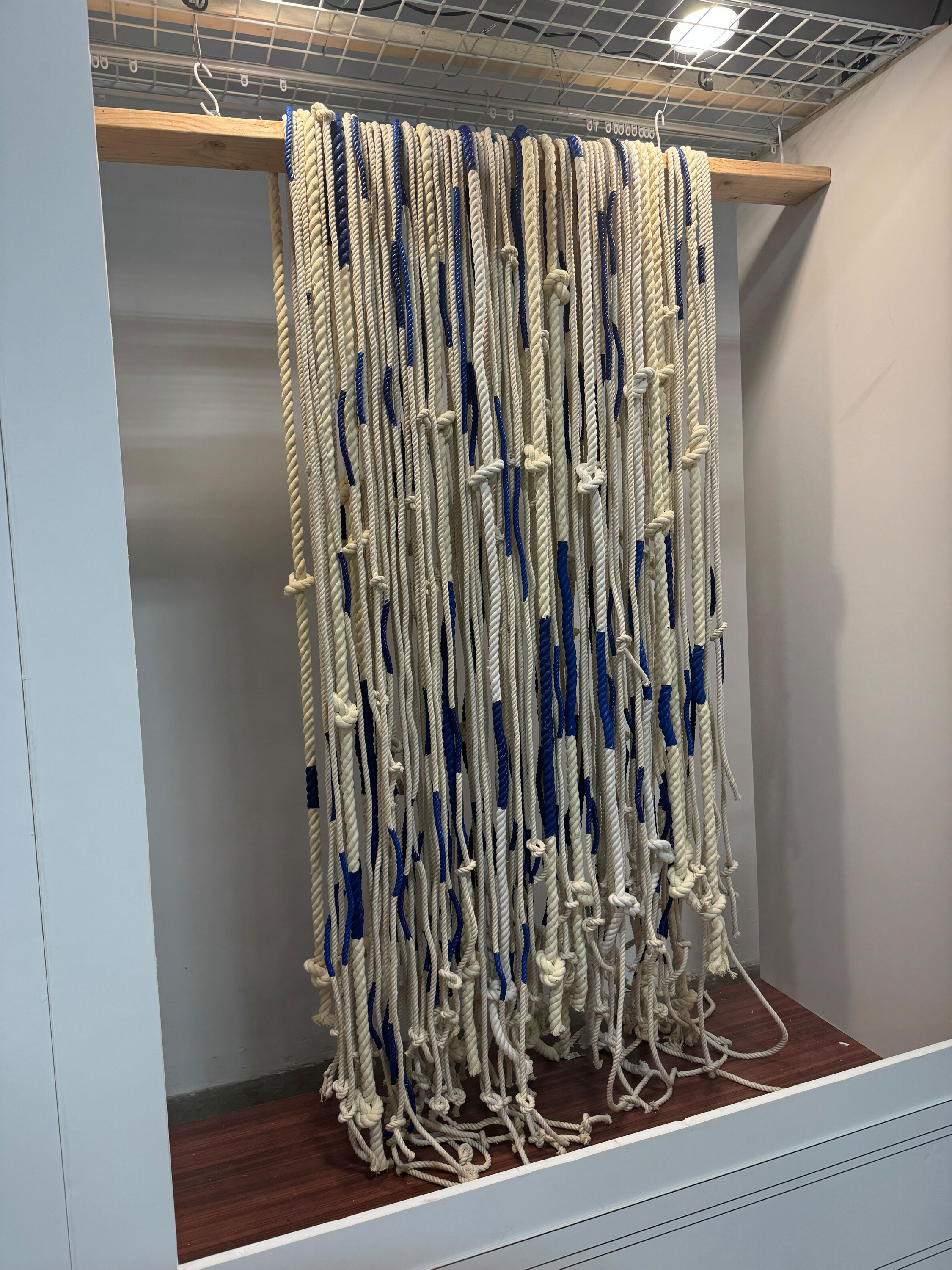 A display of hanging ropes of different lengths and thicknesses, with blue and white colors, mounted on a wooden and metal structure.