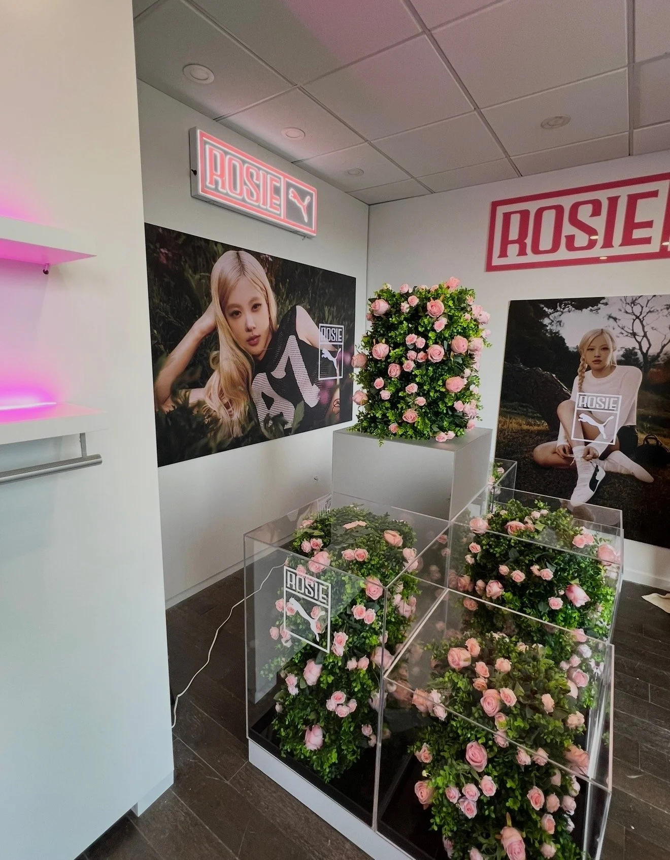 The image shows a retail display area with large posters of a blonde woman posing with a Puma shoe, pink roses arranged in clear display cases, and signs with the brand name 'Rosie' with the Puma logo.