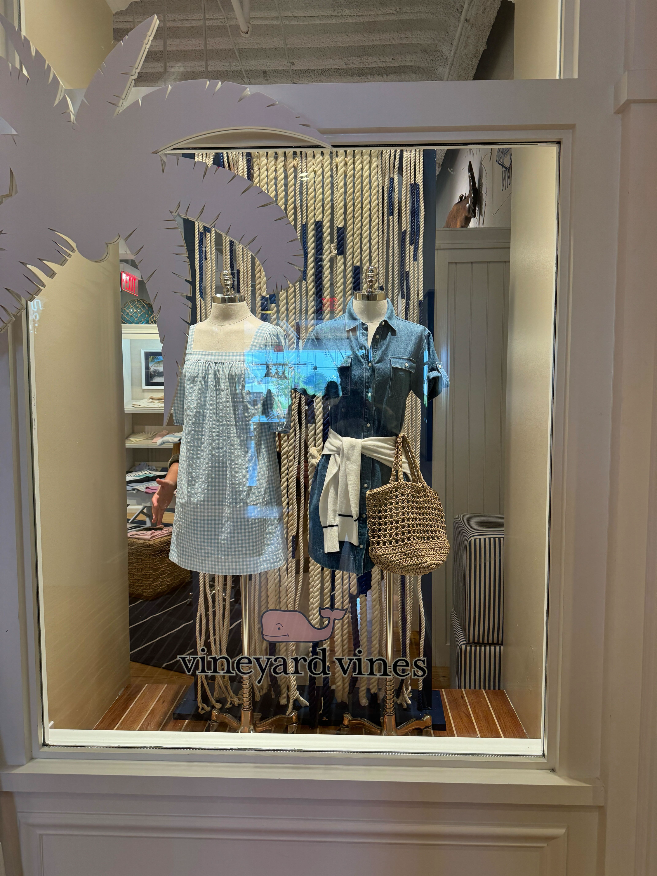 Displays mannequins dressed in casual outfits, with a backdrop of nautical rope and a sign reading 'vineyard vines' inside a store window.
