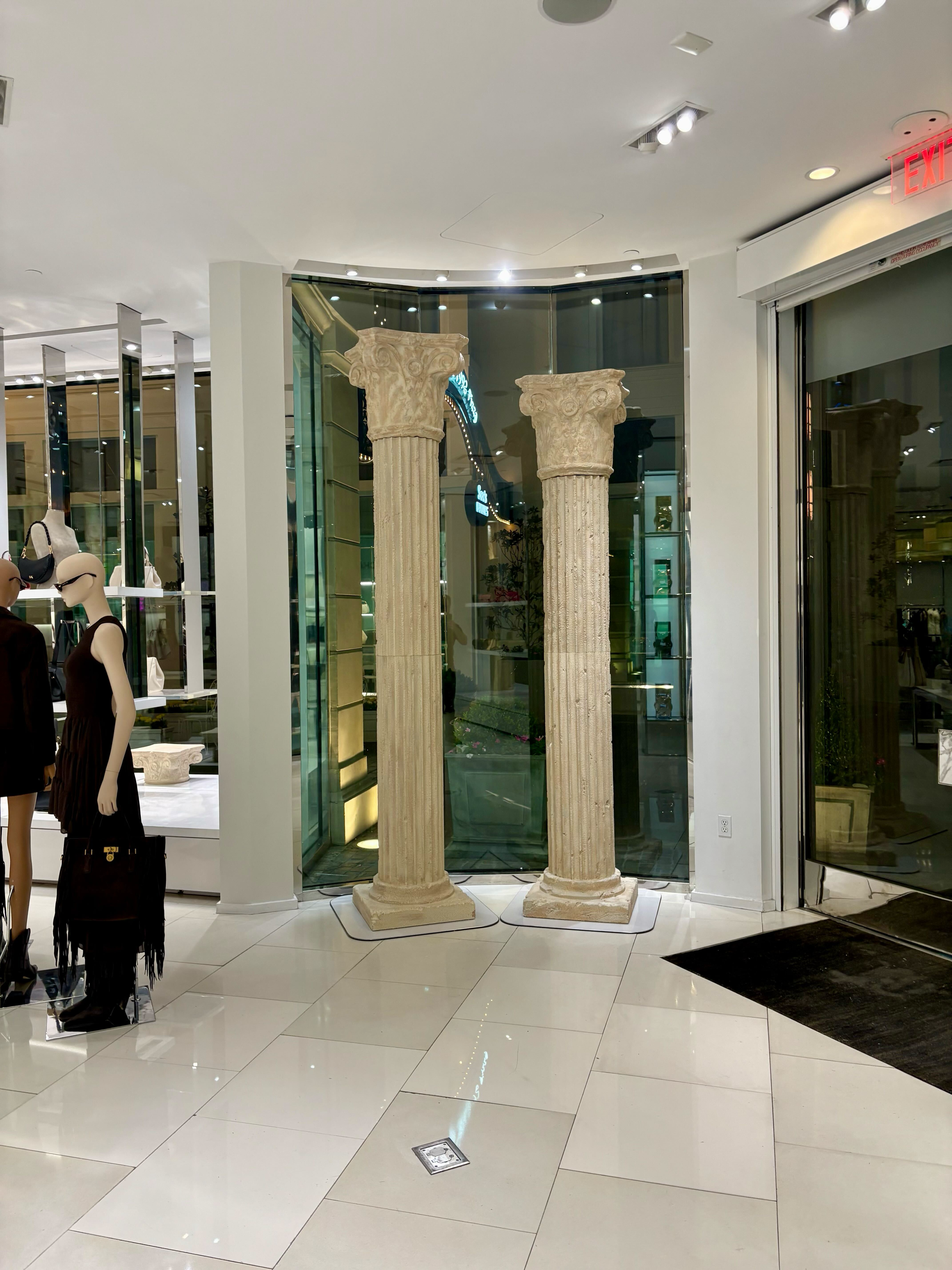 Two ancient stone columns inside a shopping mall, with mannequins displaying clothing in the background.