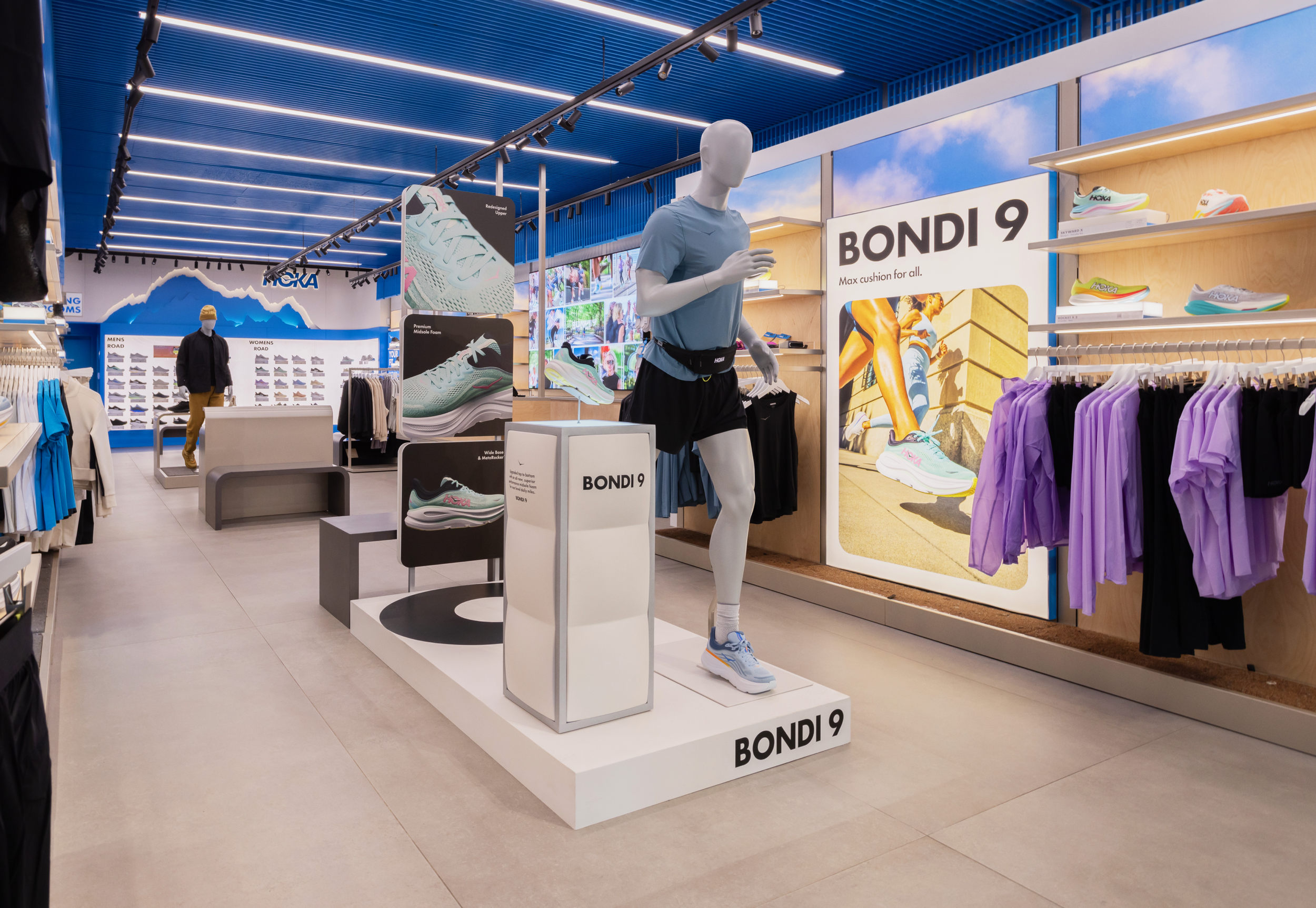 Display of Nike running shoes and athletic apparel in a retail store, with a mannequin dressed in a blue shirt and black shorts, and signage promoting Bondi 9 shoes.