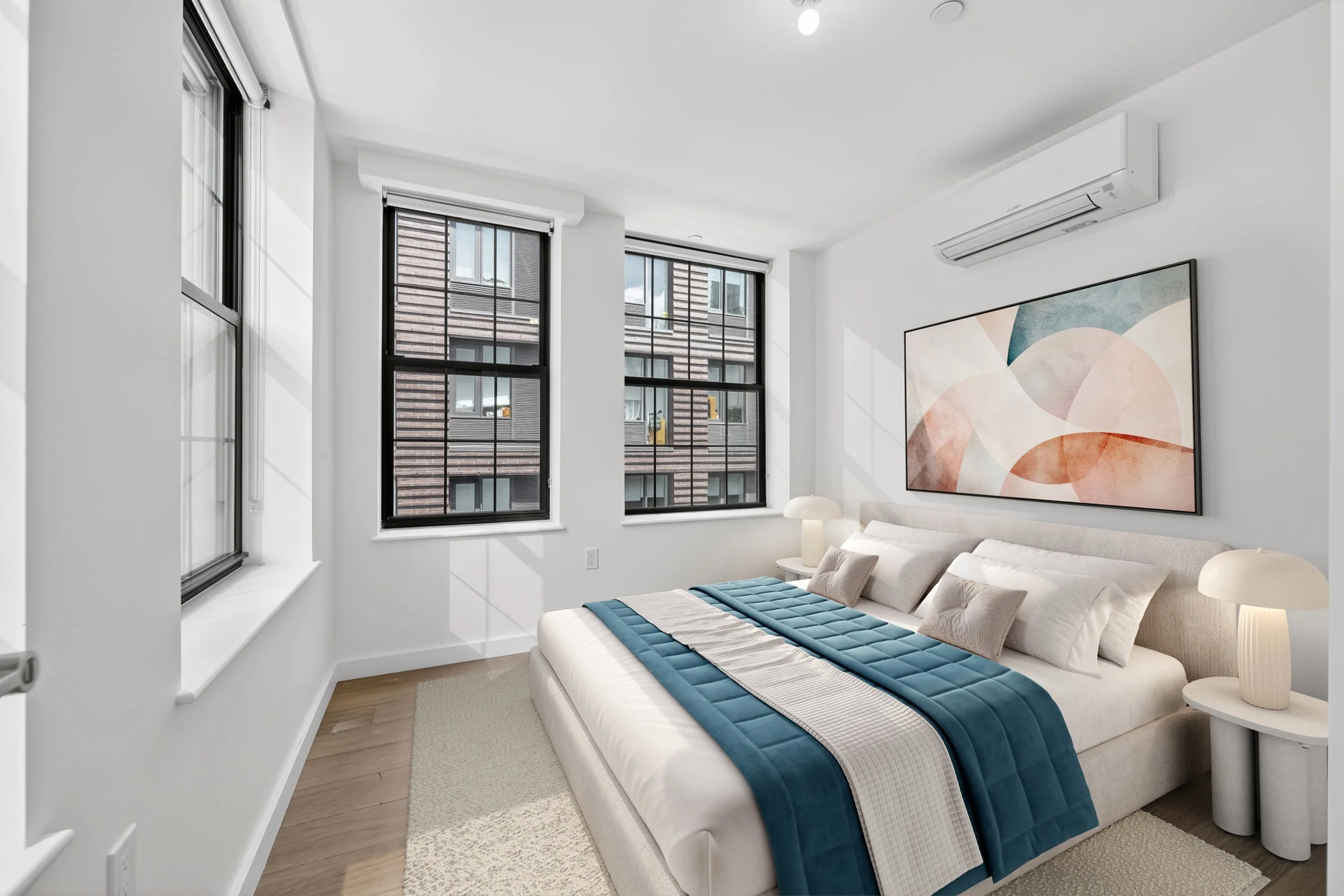 A modern bedroom with large windows, white walls, a white bed with blue and beige bedding, and abstract wall art.