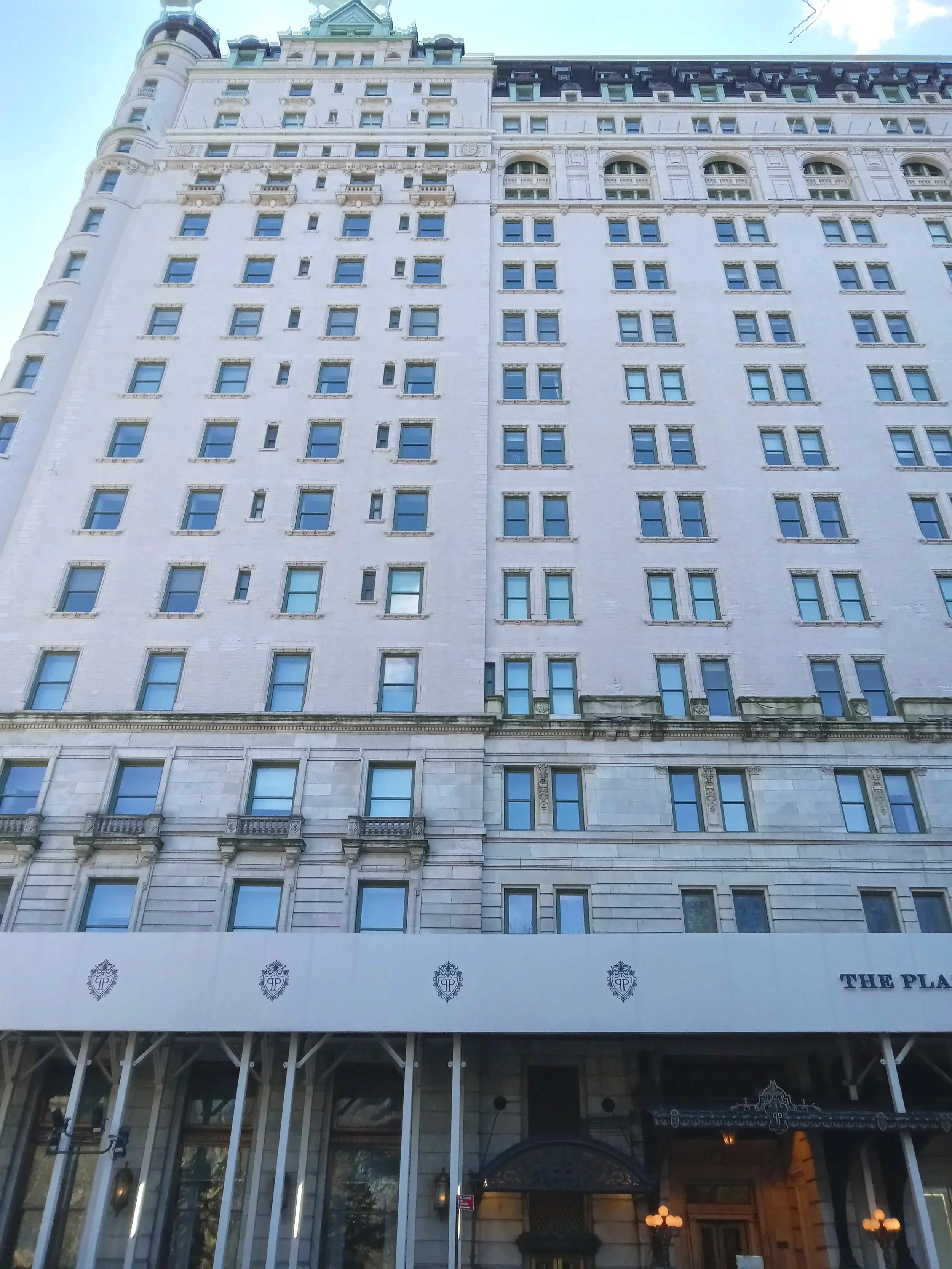 View of a tall, historic white building with numerous windows, ornate architectural details, and a restaurant entrance at the bottom with decorative lighting and signage.