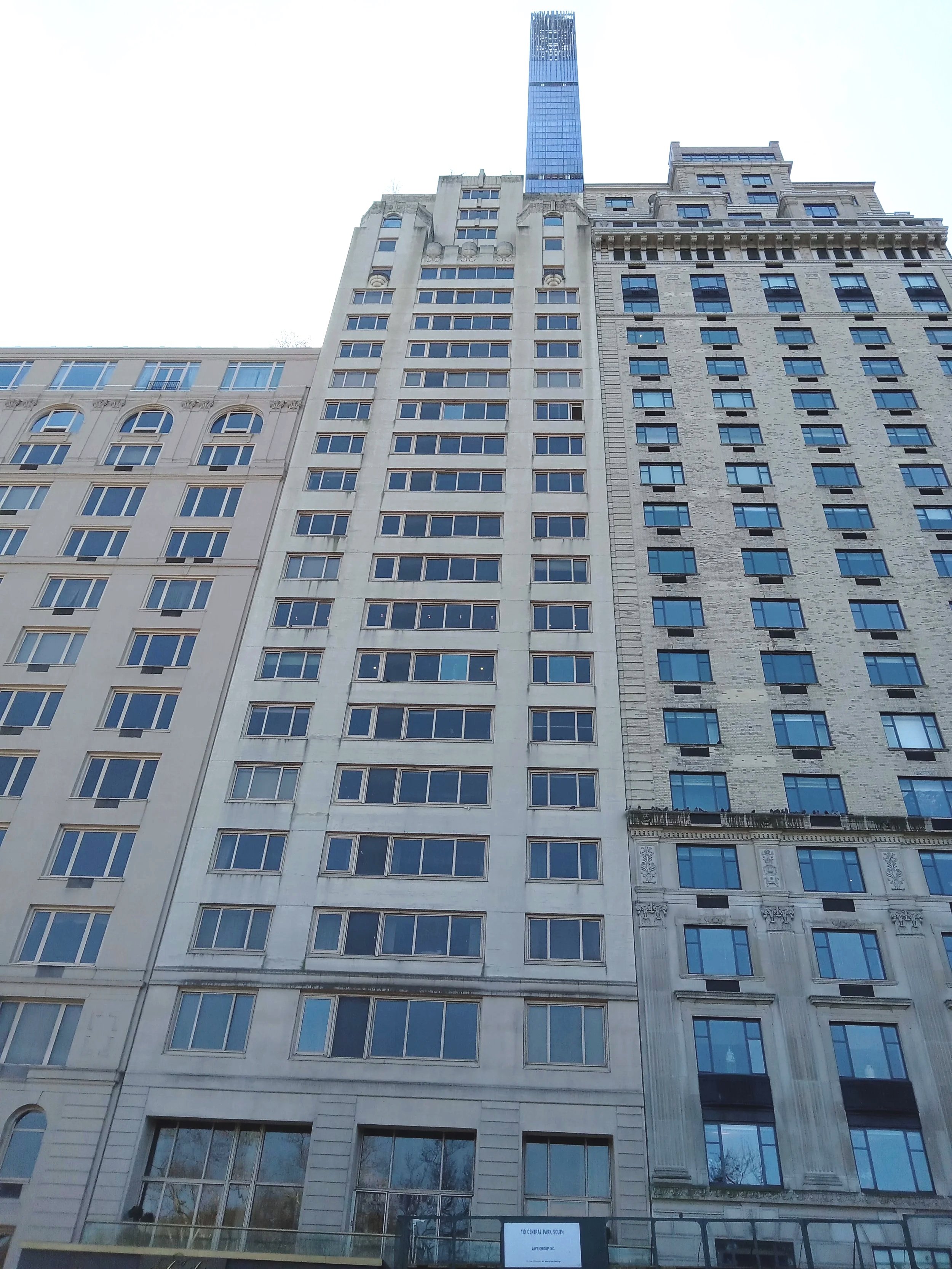 A tall, blue glass skyscraper behind historic beige and gray buildings with numerous windows, taken from street level.