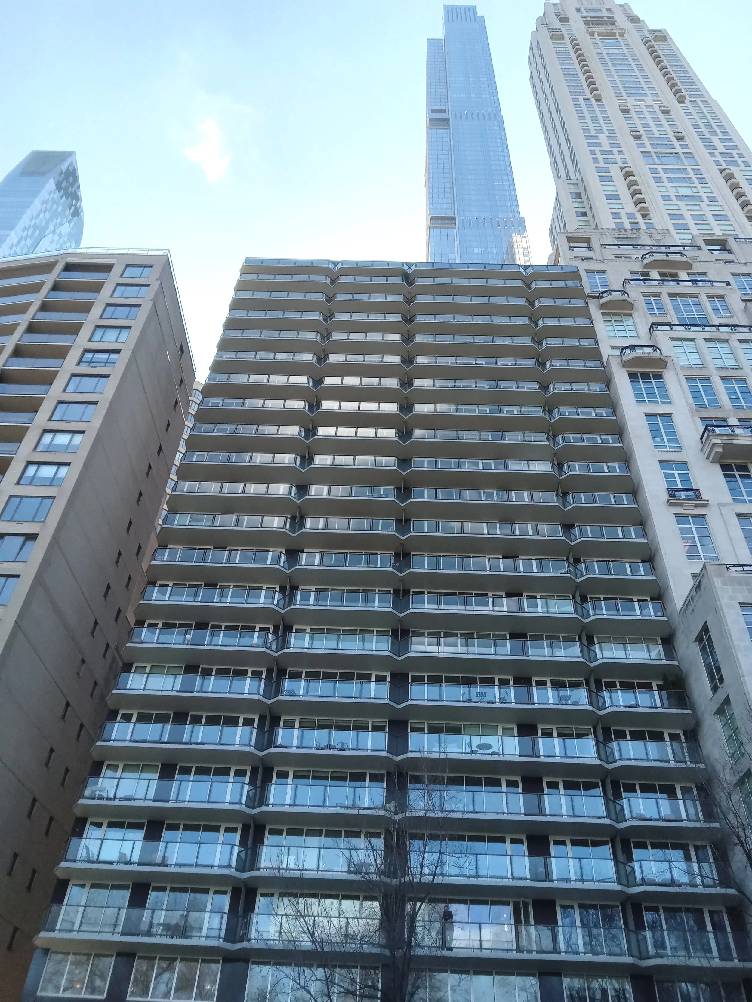 View looking up at tall modern glass skyscrapers and apartment buildings with balconies against a clear sky.