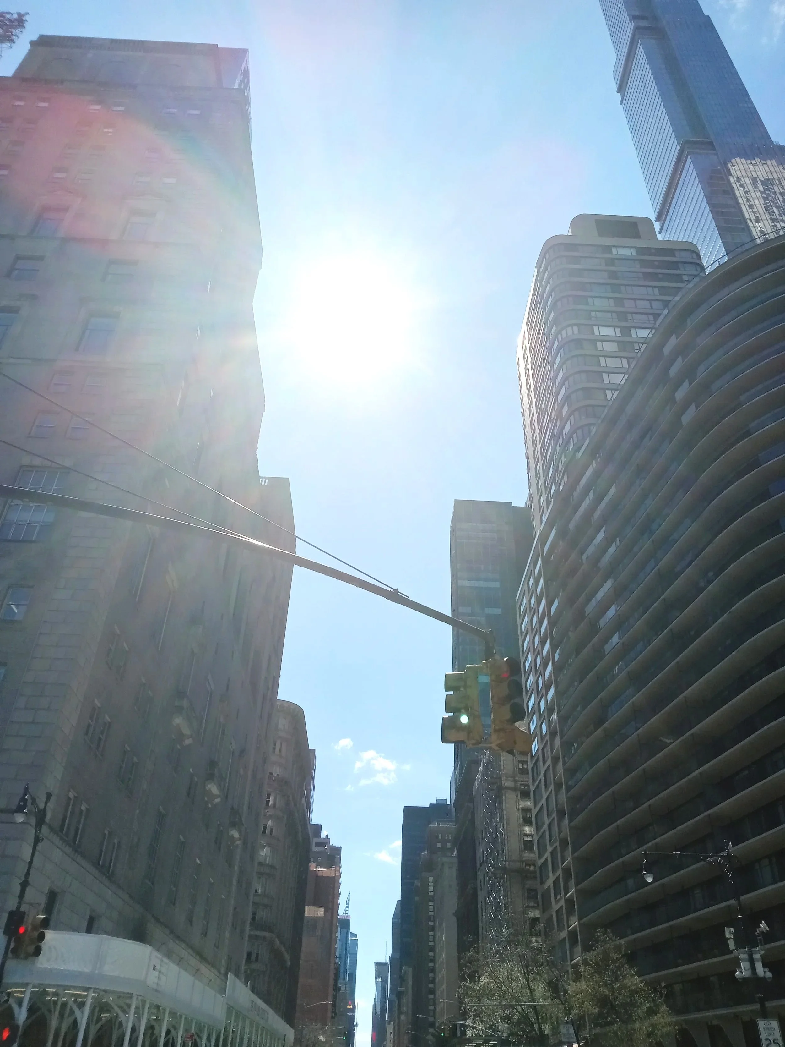 Looking up at tall skyscrapers on a city street with a clear blue sky and sunlight.