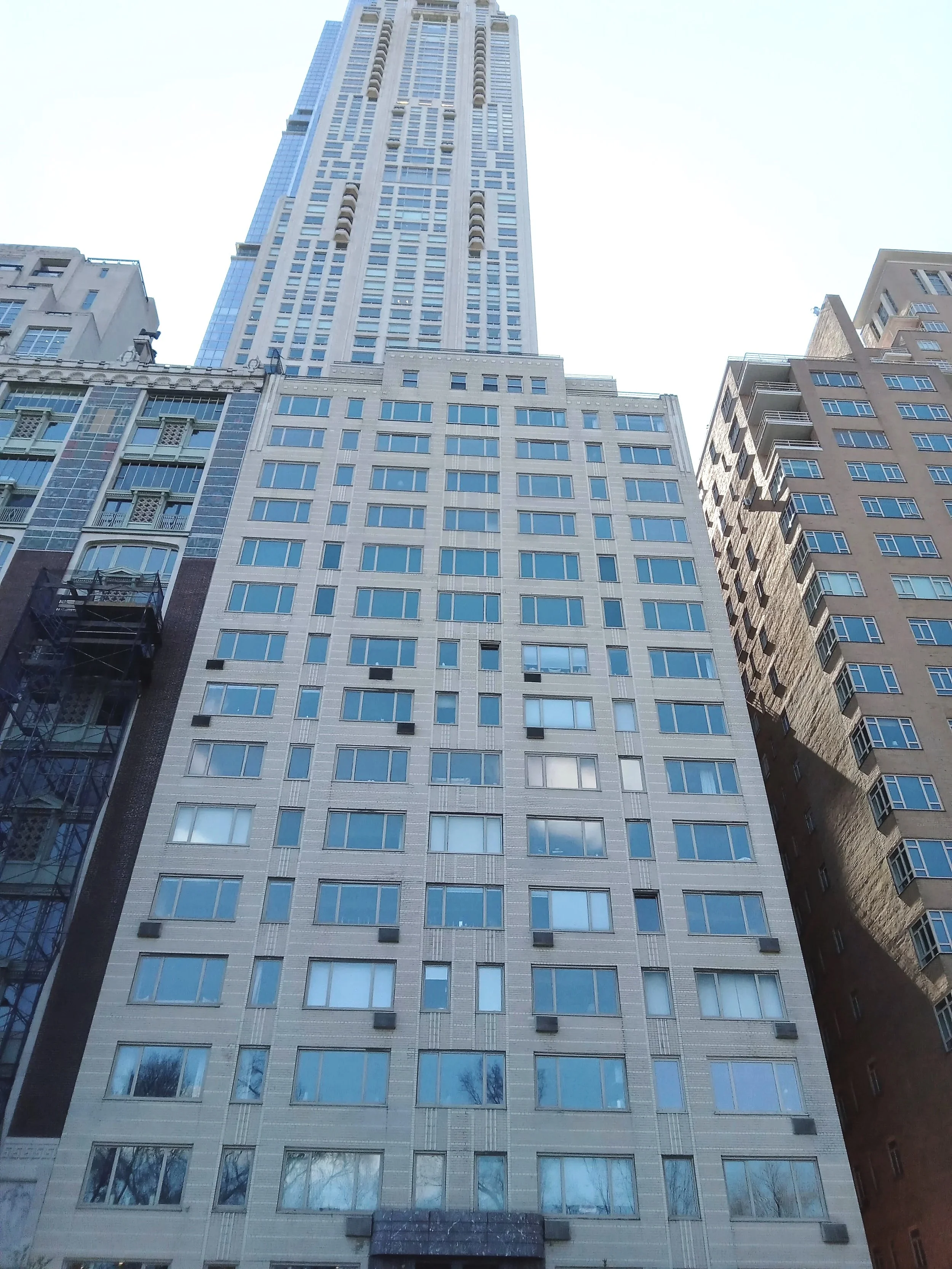 A tall skyscraper viewed from the ground with a blue sky in the background, surrounded by other high-rise buildings.