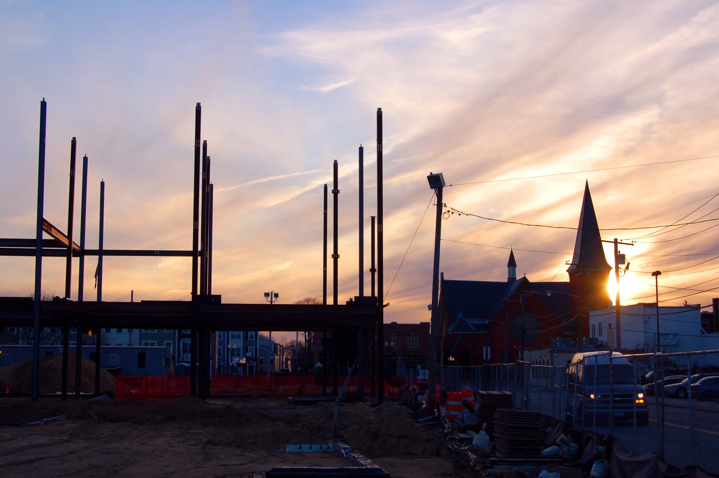 Construction site during sunset with partially built structure, construction materials, and power lines in the background.