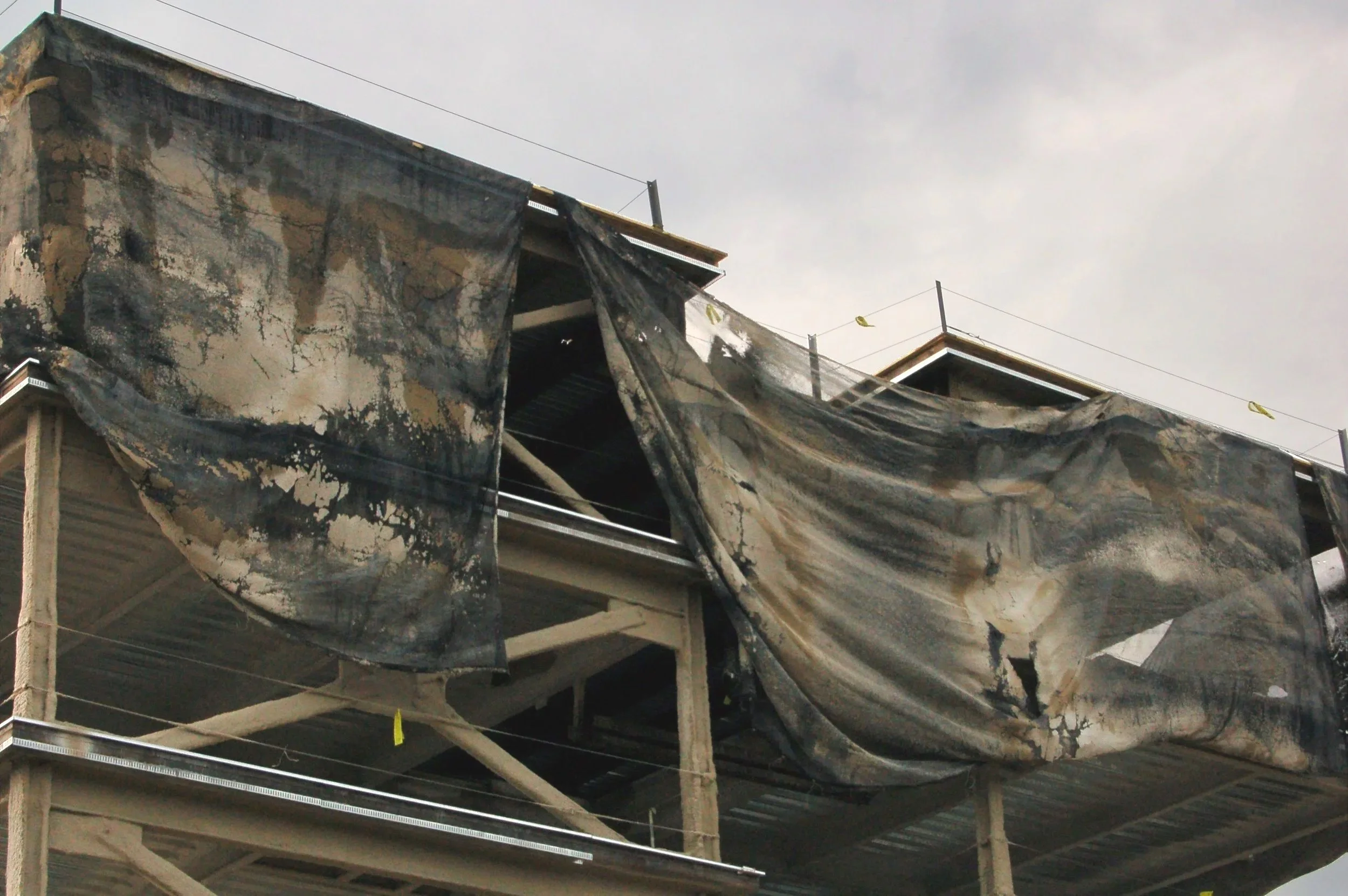 Burned section of a building with tarps covering the area and construction materials visible underneath.