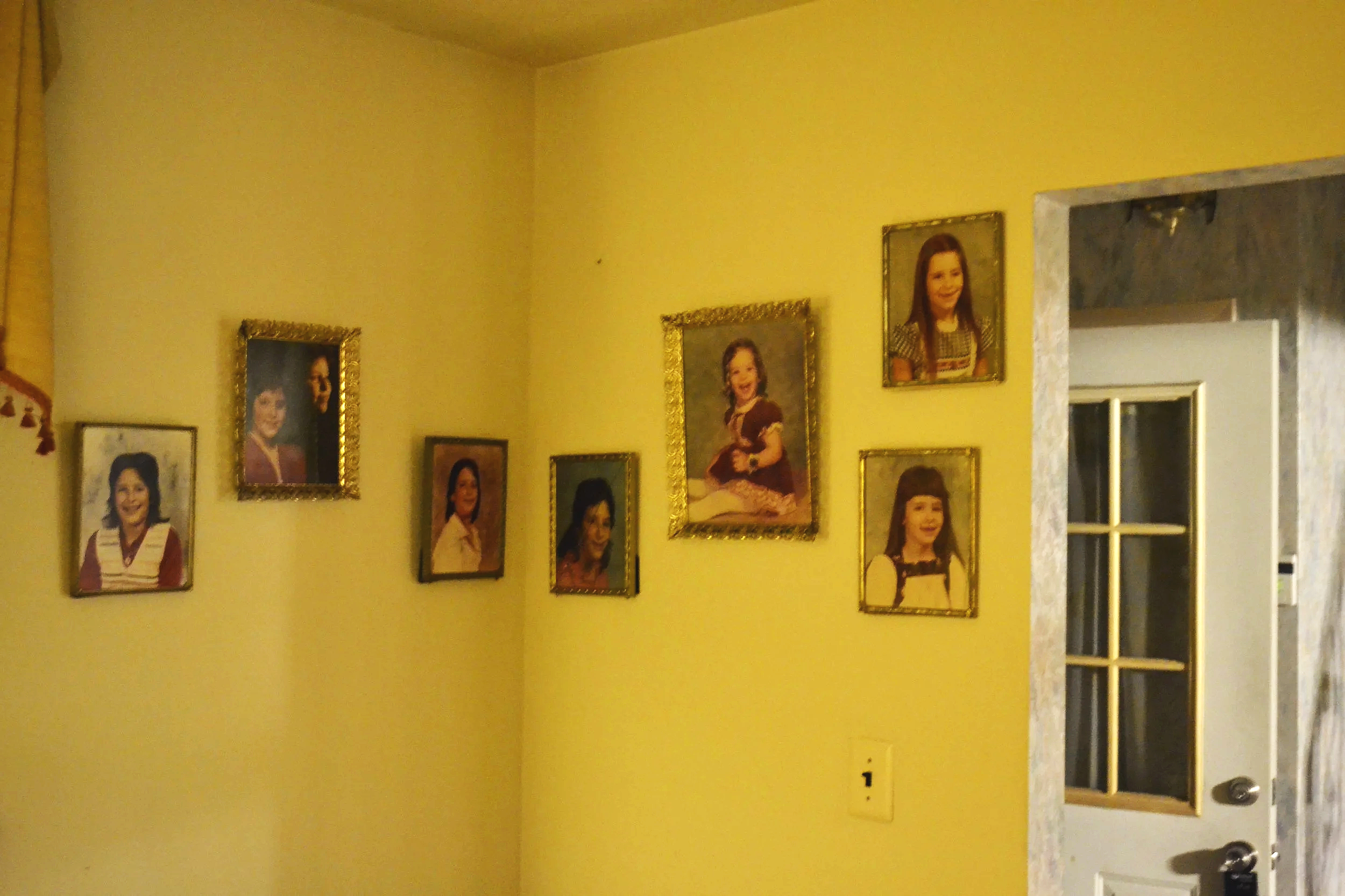 A yellow wall decorated with framed family portraits of a young girl, in various sizes and styles, with a doorway on the right side.