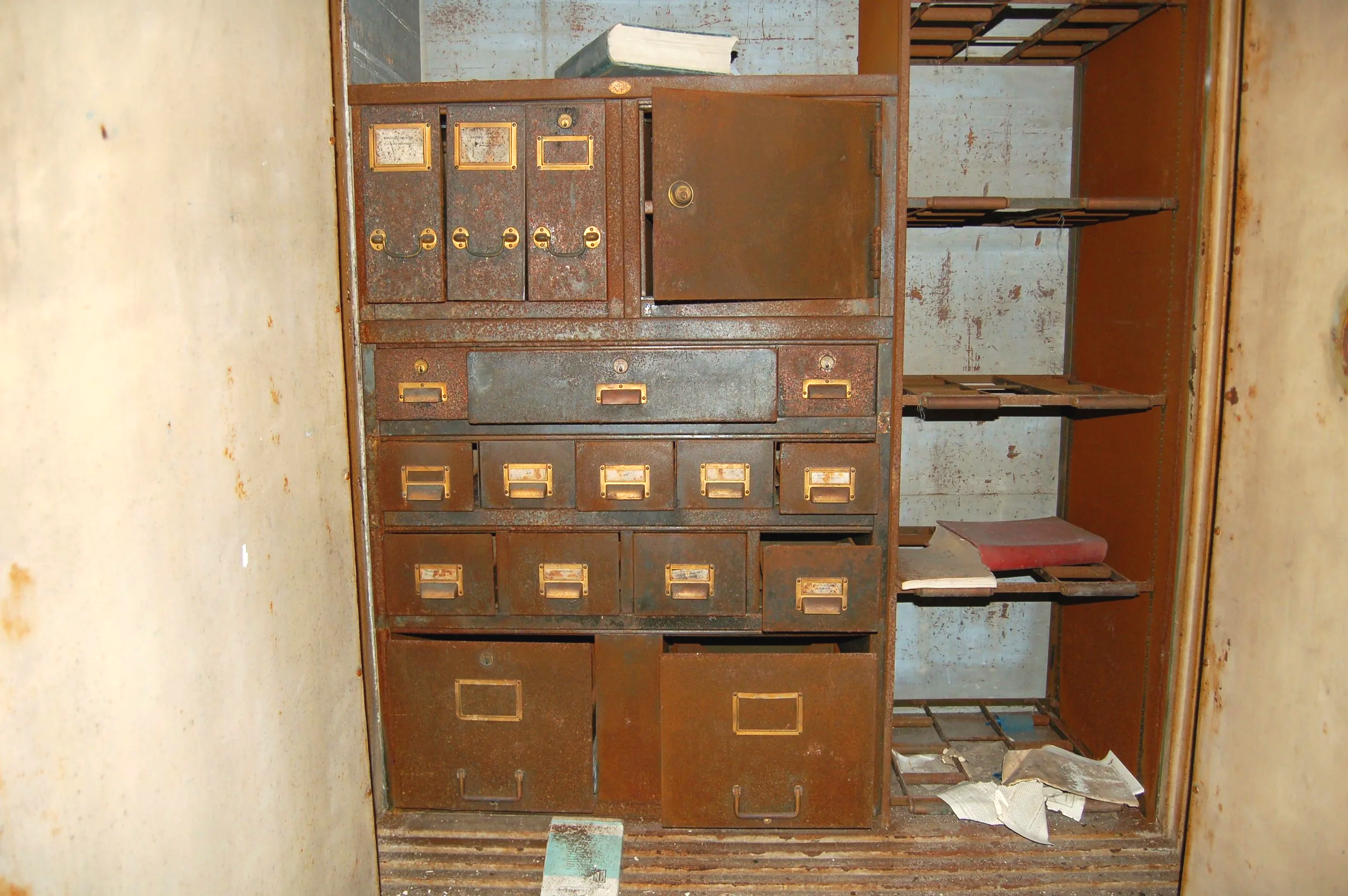 An old, rusty metal locker with multiple compartments and faded labels, situated in a worn, dusty room with peeling paint.