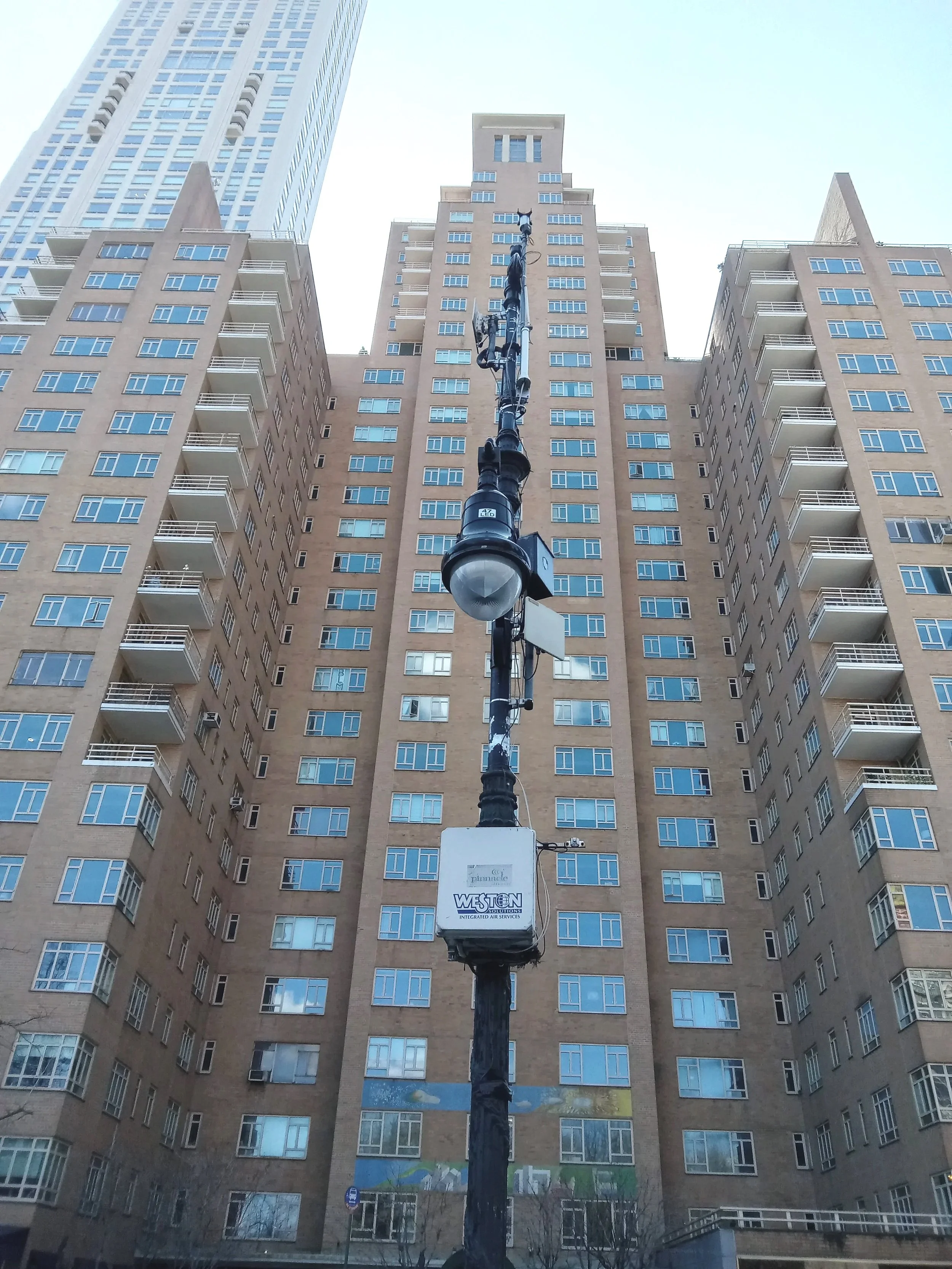 View of tall residential buildings with many windows and balconies, seen from below, with a street lamp in the foreground and a sign on the street pole.