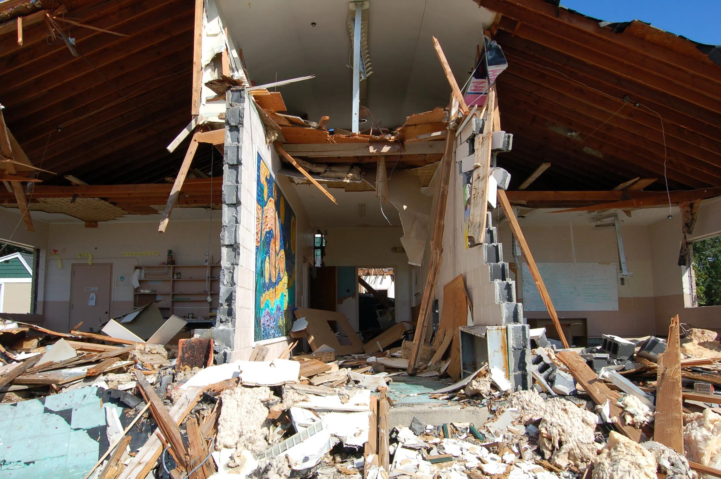 The interior of a building that has been heavily damaged or demolished, with debris, broken walls, and exposed wooden beams.