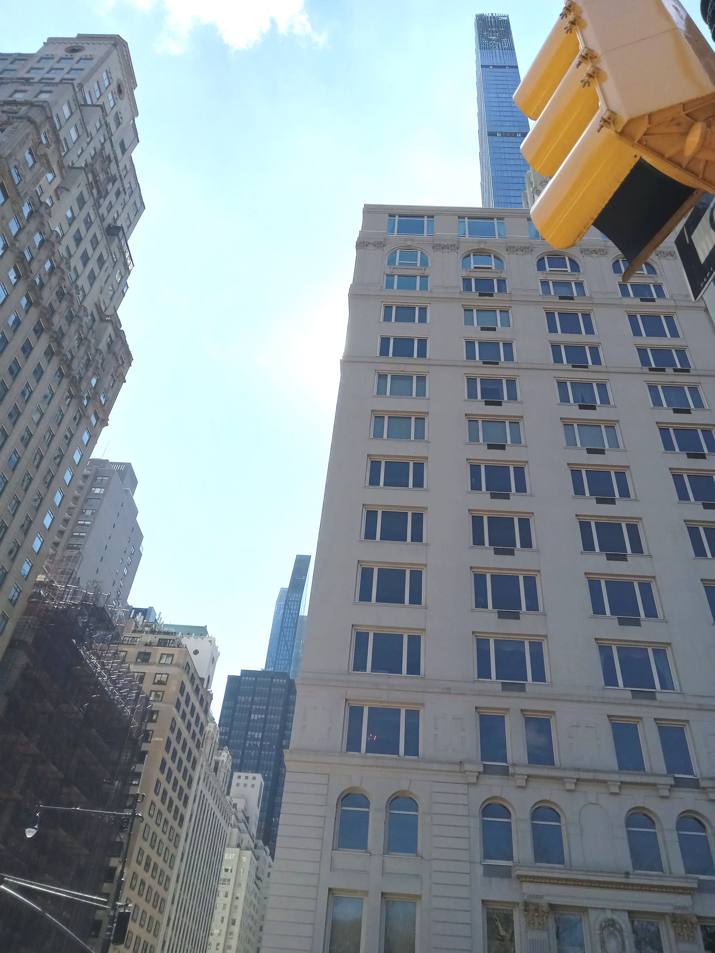 Skyscraper buildings in a city with a mostly clear blue sky and some clouds, showing a mix of modern and older architecture.