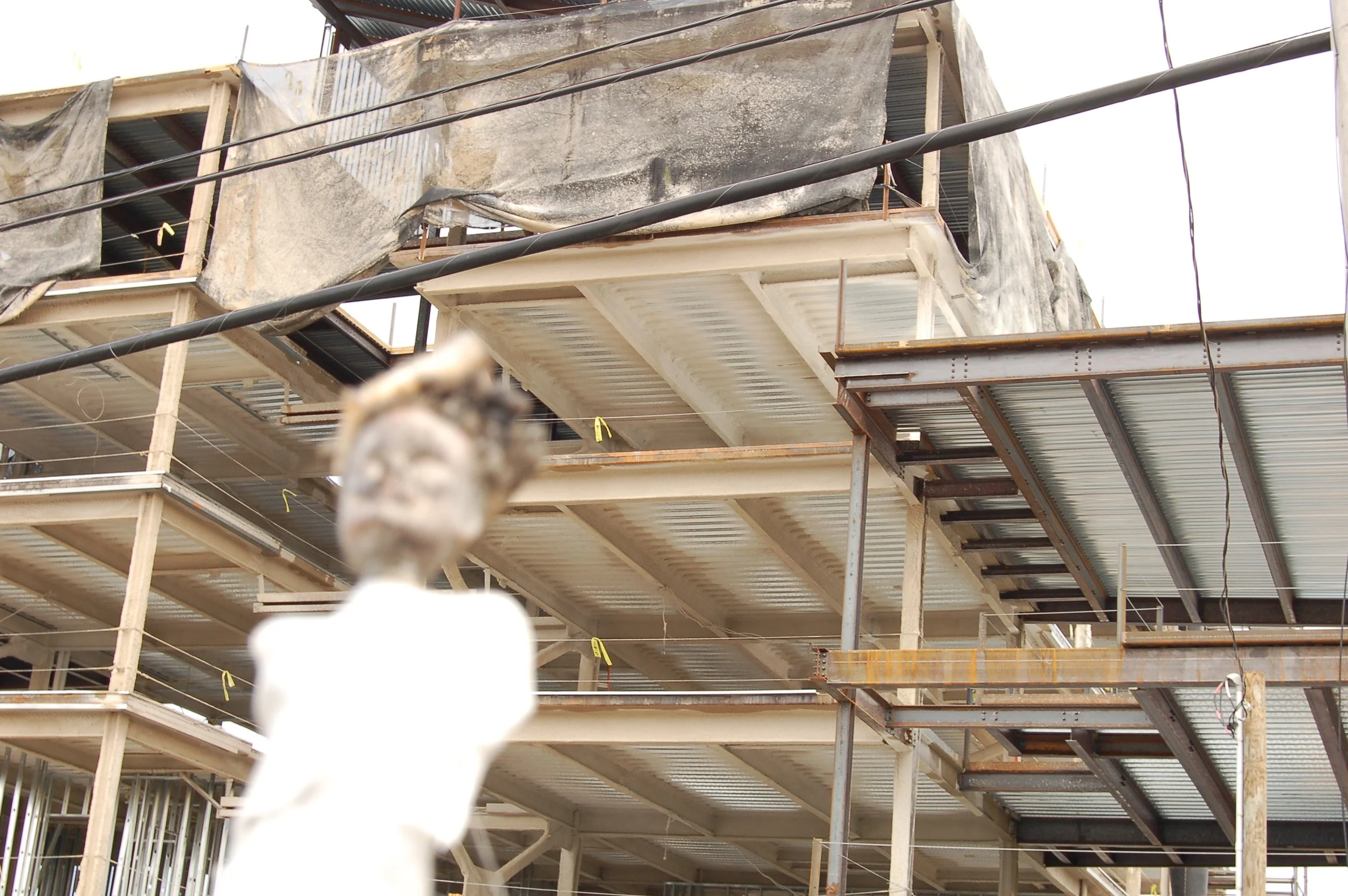 Construction site with partially built multi-story buildings, exposed metal framework, and weathered tarps or protective covers draped over the structures, seen from below.