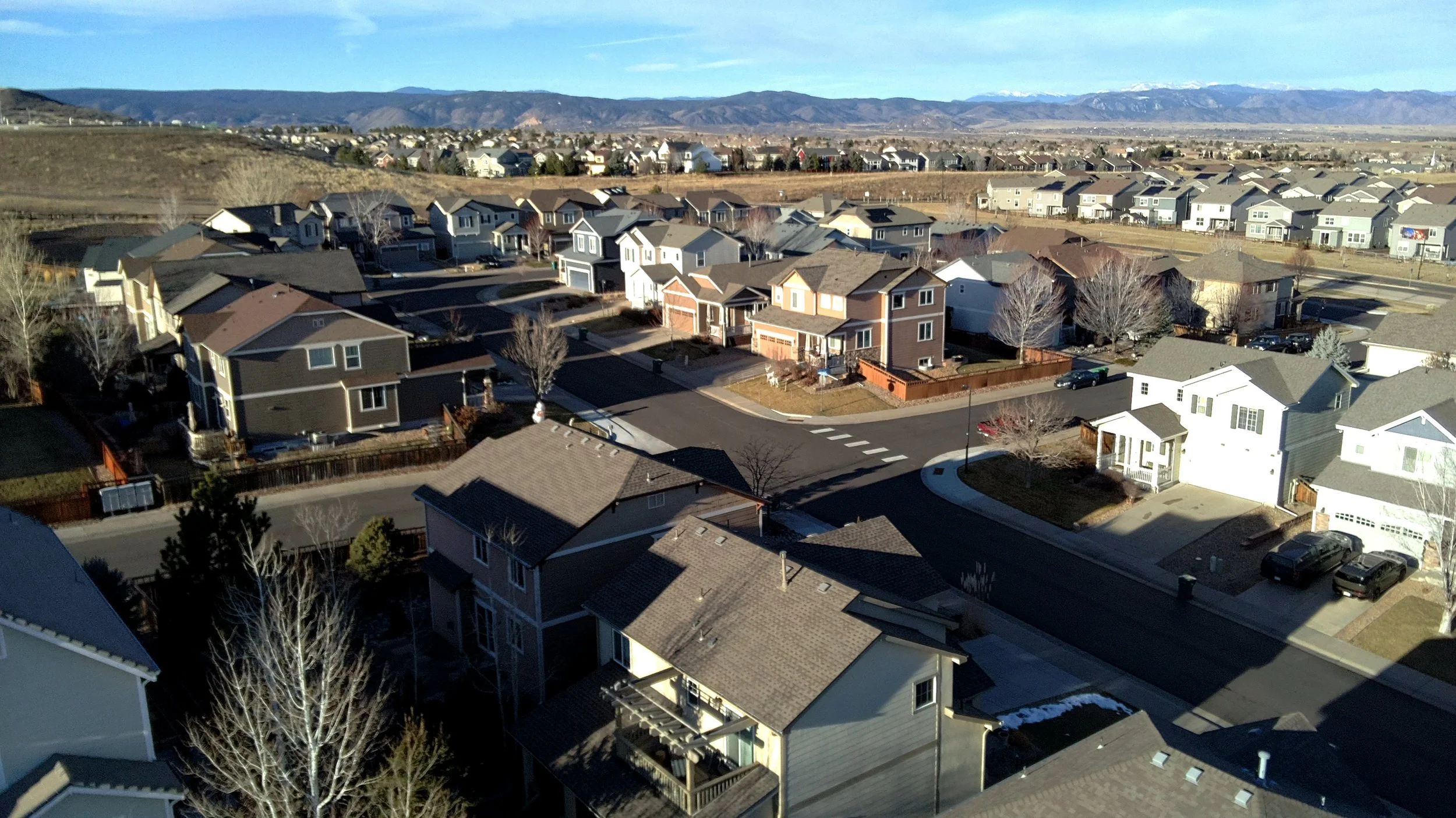 Aerial view of a suburban neighborhood with numerous houses, roads, and trees, with mountains in the background on a clear day.