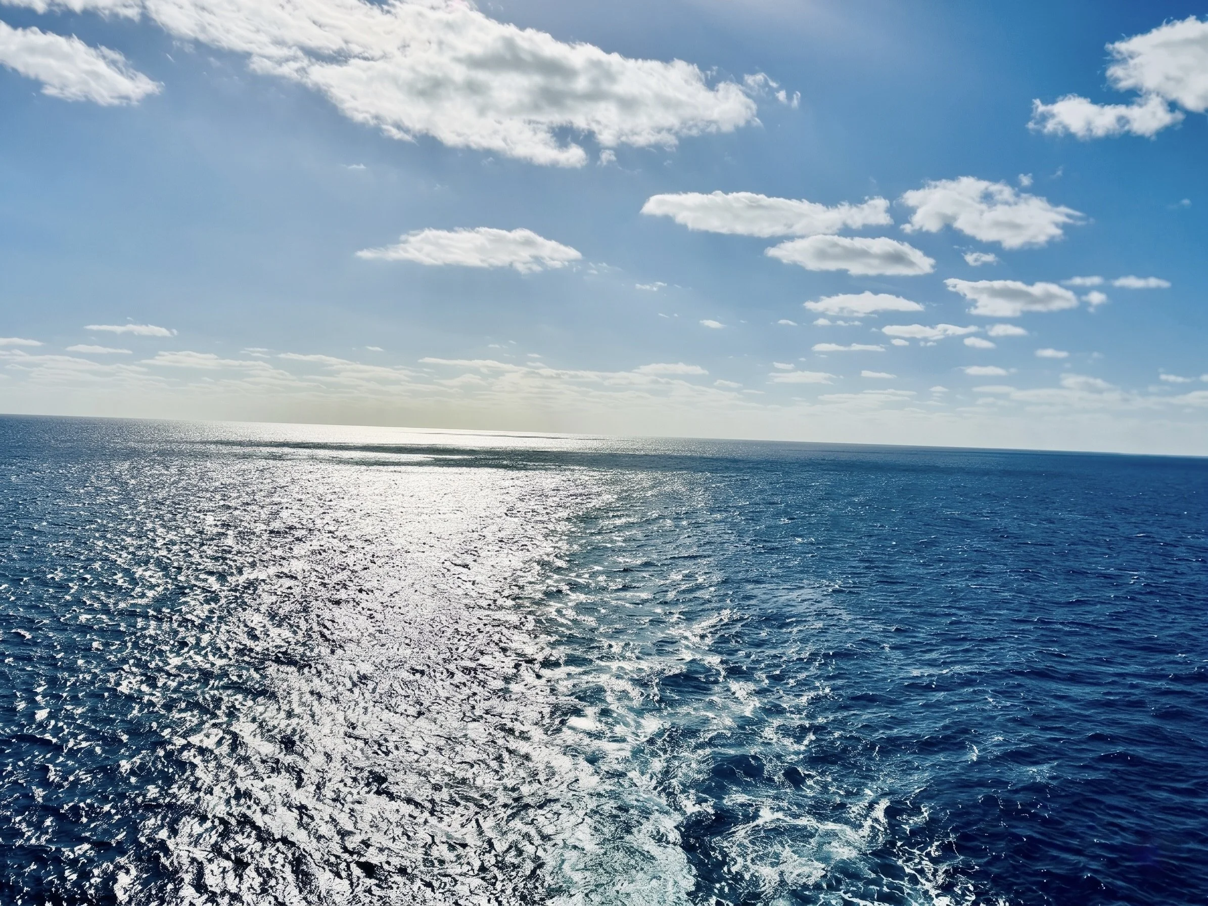 Ocean water with sunlight reflection and a partly cloudy sky.