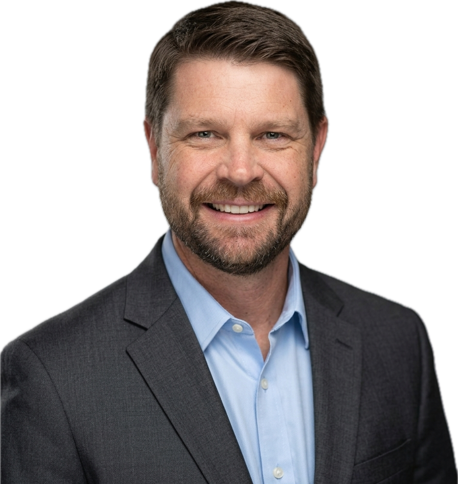 A smiling man with brown hair and a beard, wearing a dark suit jacket and a light blue collared shirt.