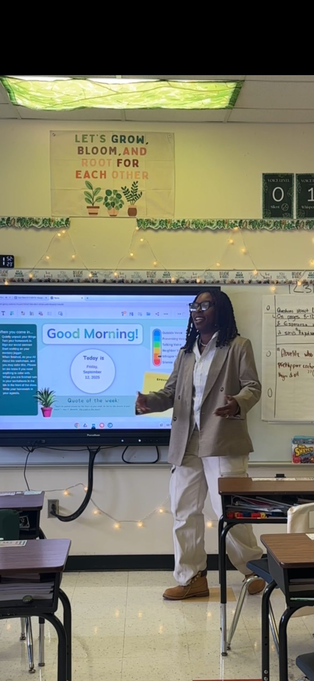 A teacher standing in front of a classroom next to a large digital screen displaying a morning message for Friday, September 12, 2025.