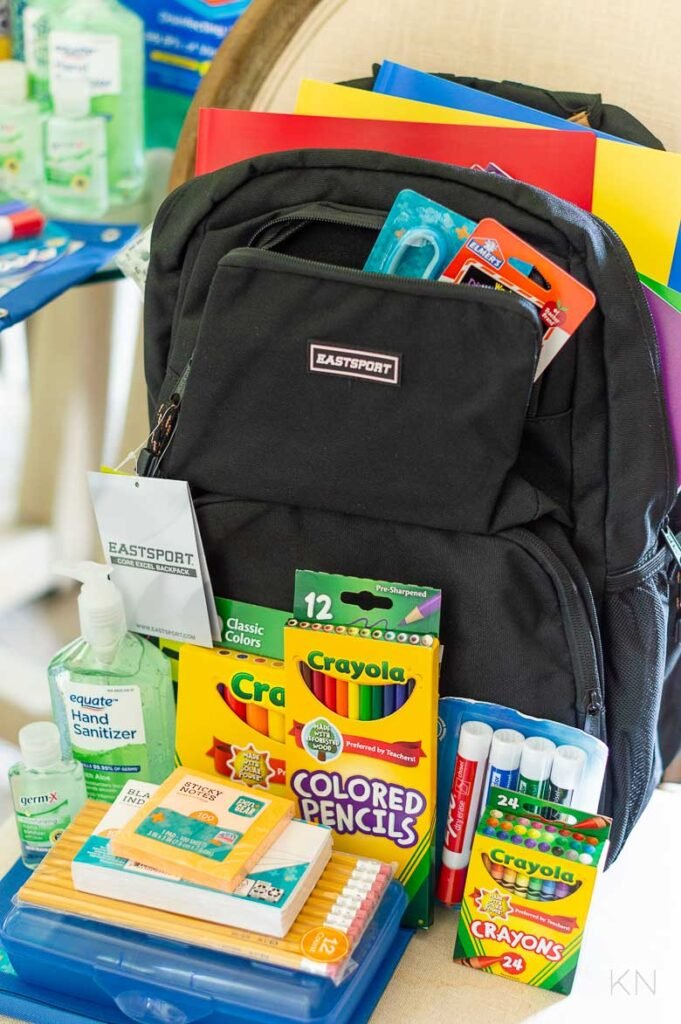 School supplies including a backpack, Crayola colored pencils, Crayola crayons, notebooks, index cards, hand sanitizer, sticky notes, and markers.