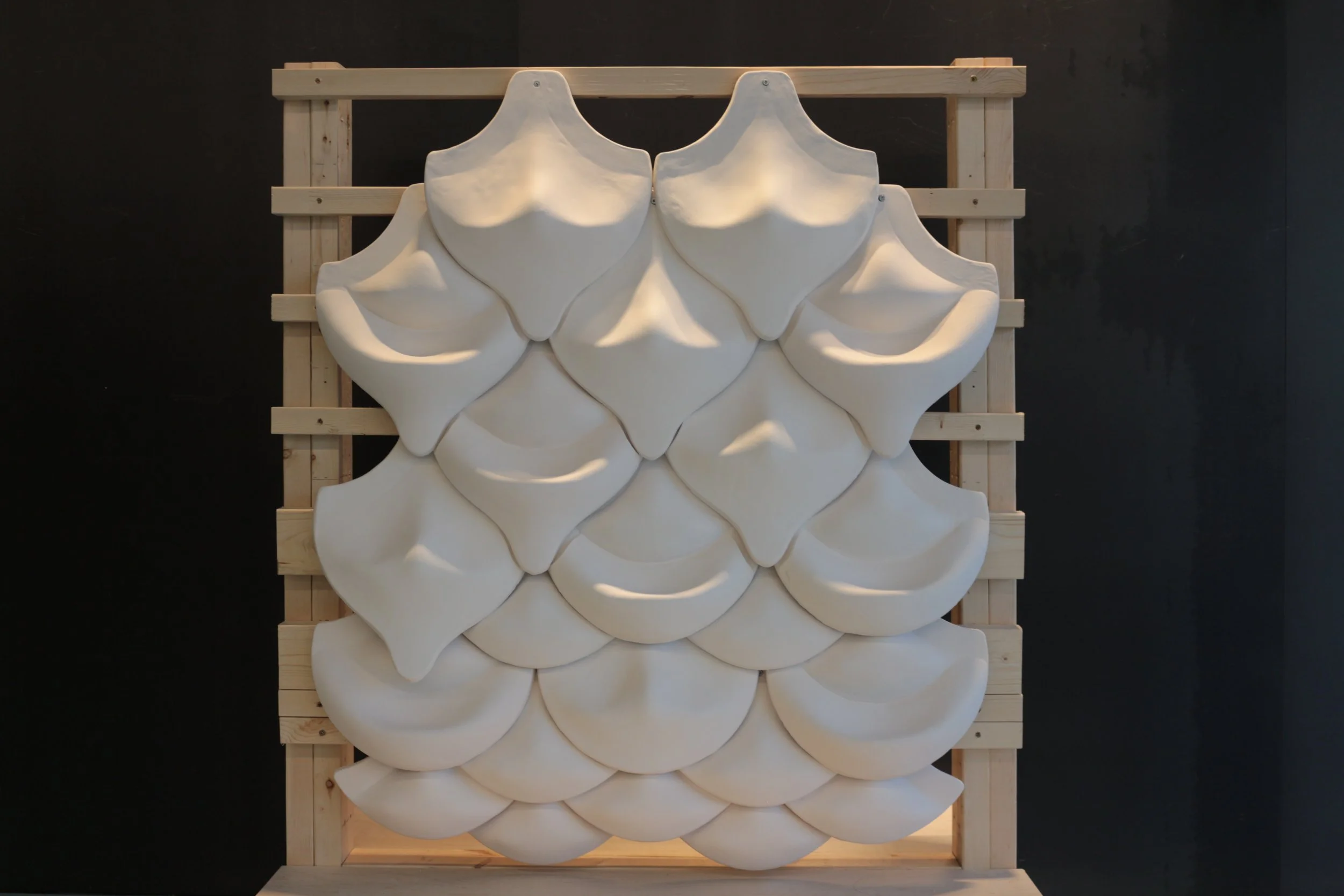 Multiple white sculpted wall tiles with leaf-like shapes mounted on a wooden frame.
