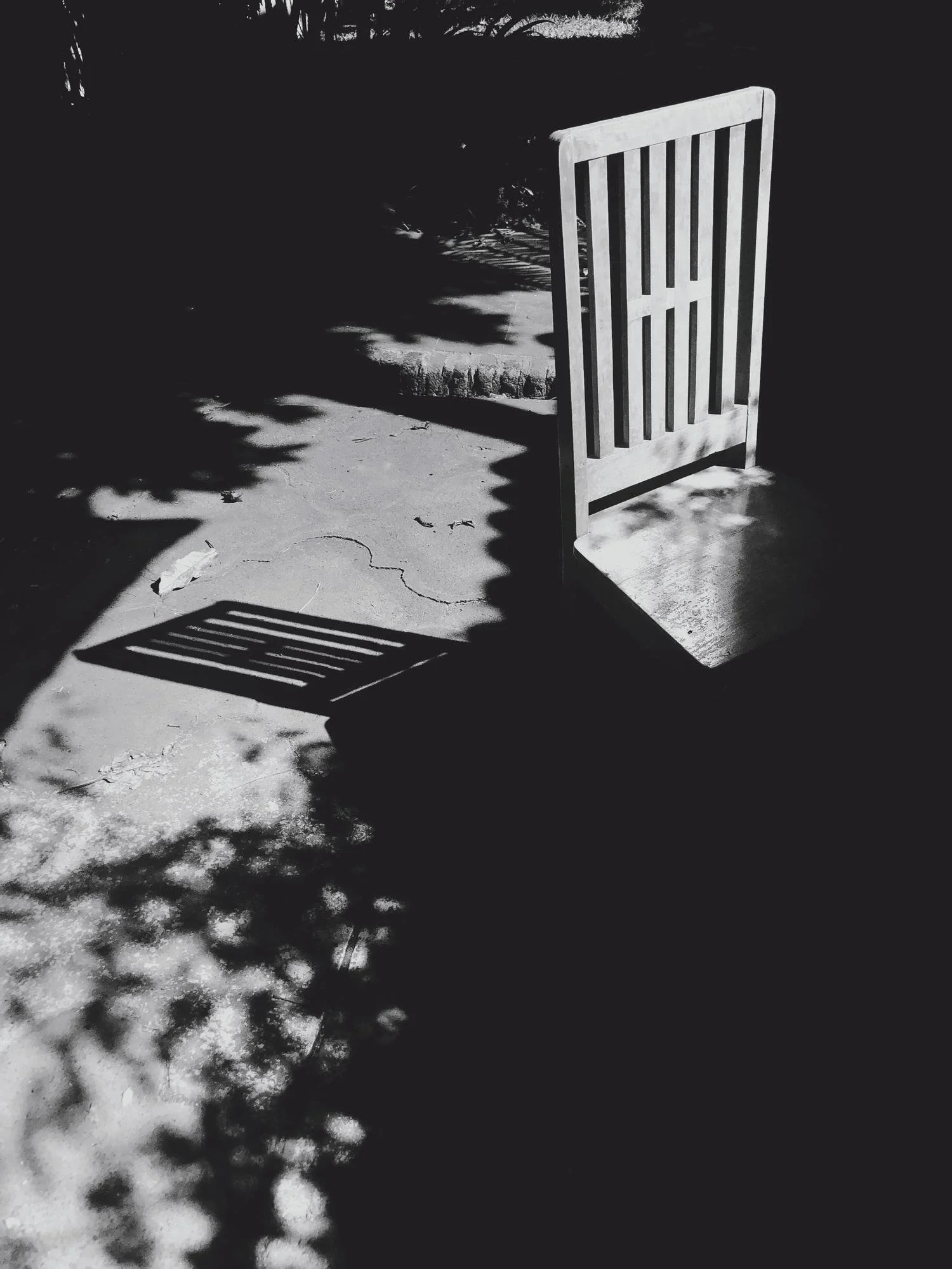 Silla de madera en un espacio exterior con sombra y textura de suelo.