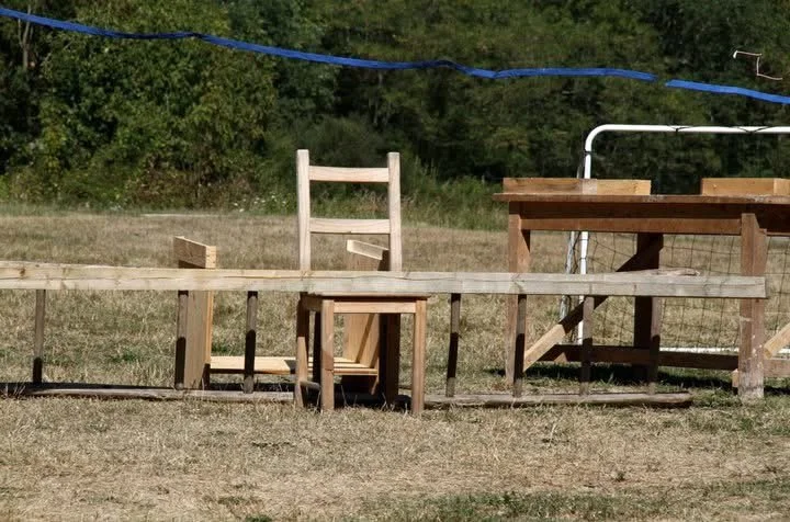 Muebles de madera en un campo, incluyendo un respaldo de silla, una mesa y otros artículos en construcción o reparación.