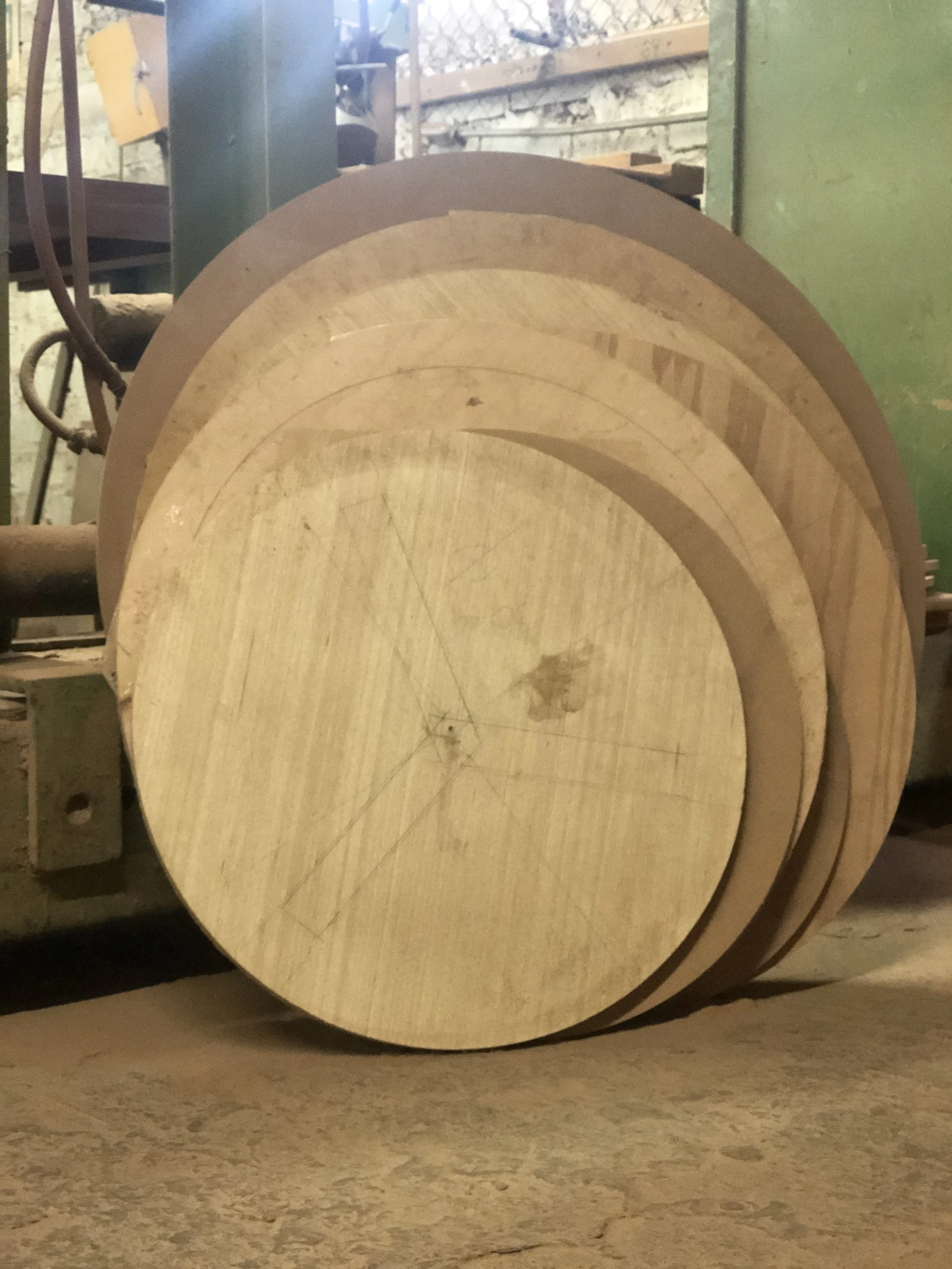 Tres ruedas de madera apiladas en un taller, con marcas y marcas de lápiz en la superficie de la madera.