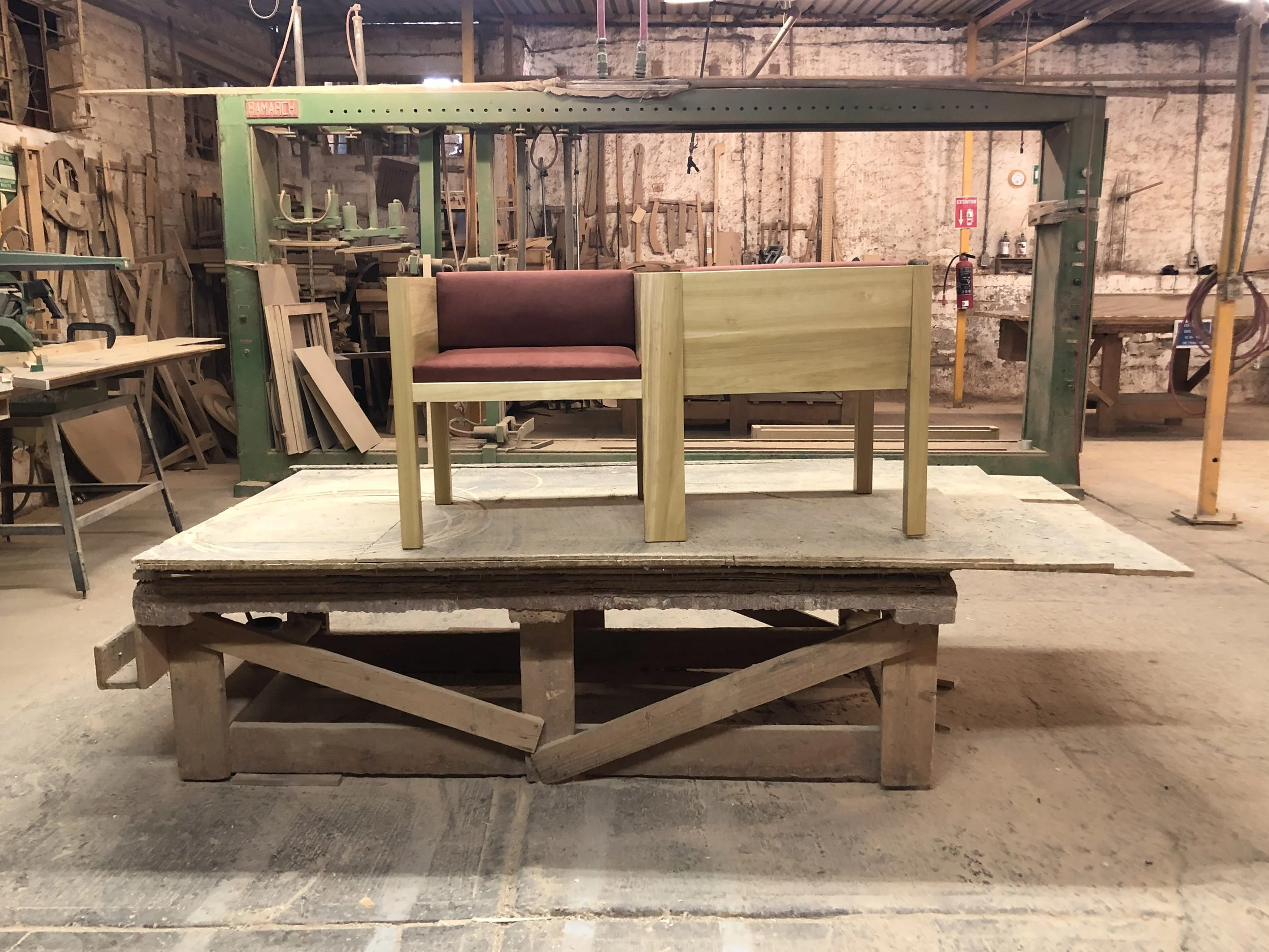 Sillón Yo -Tú para dos. Carpintería con maquinaria para trabajar madera y un mueble en proceso de fabricación.