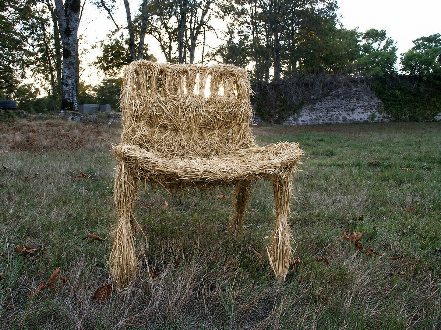 Silla hecha con paja en un campo con árboles y muro de piedra al fondo