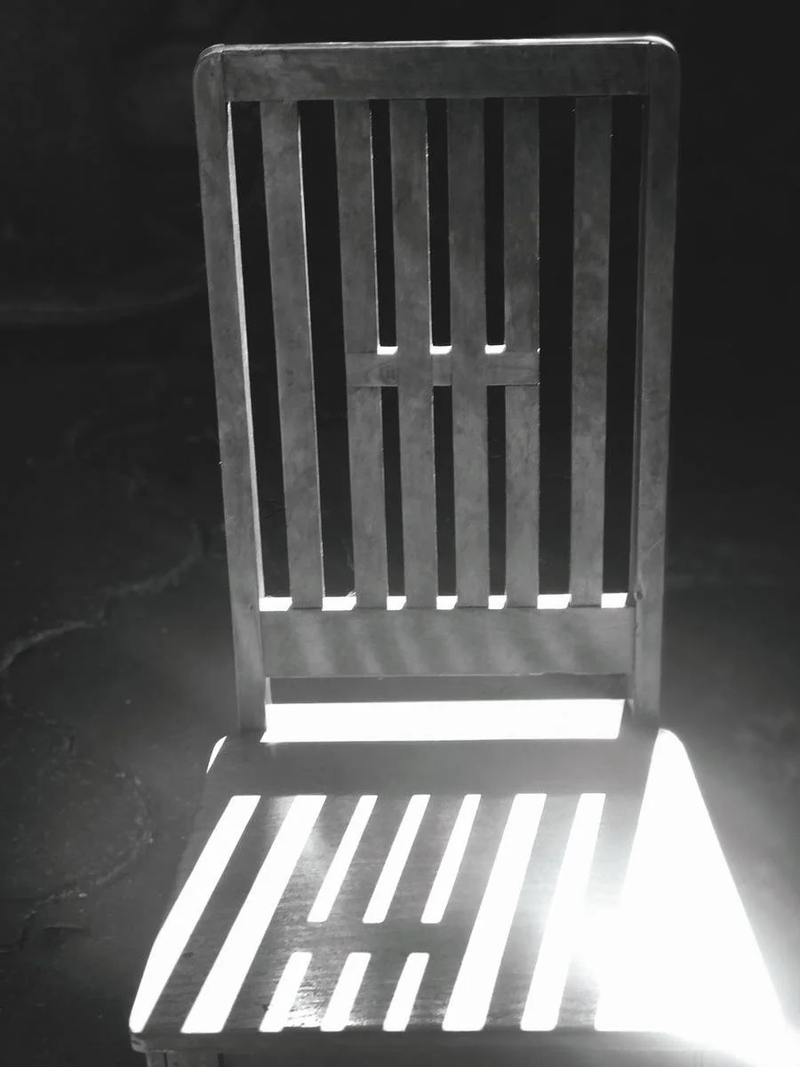 Silla de madera con sombras y luz que crea un patrón en el suelo.