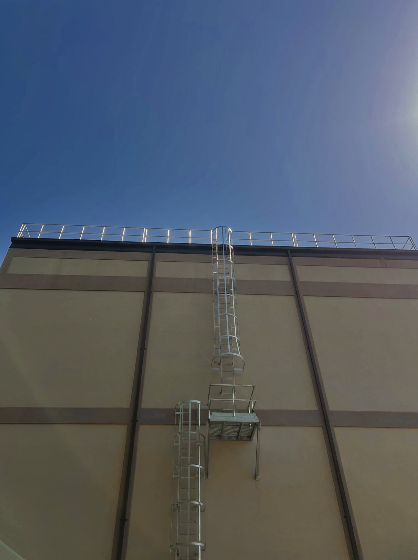 Yellow exterior of a building with a ladder and safety railing on the roof against a clear blue sky.