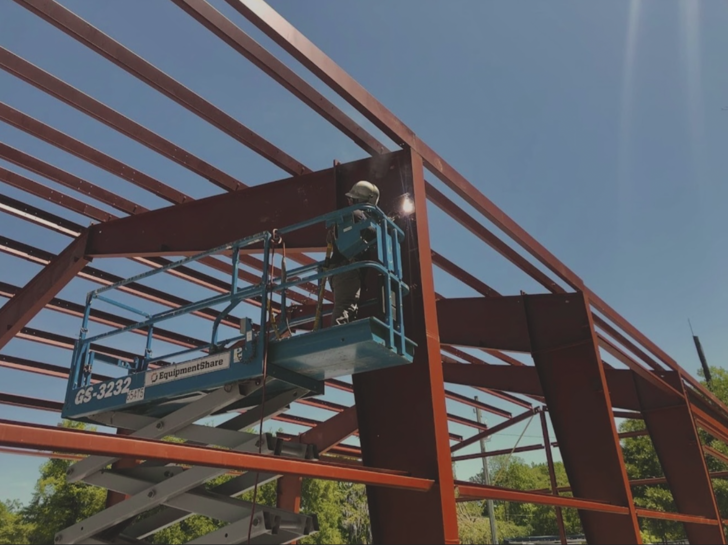 A construction worker on a lift working on the steel framework of a building during the daytime.